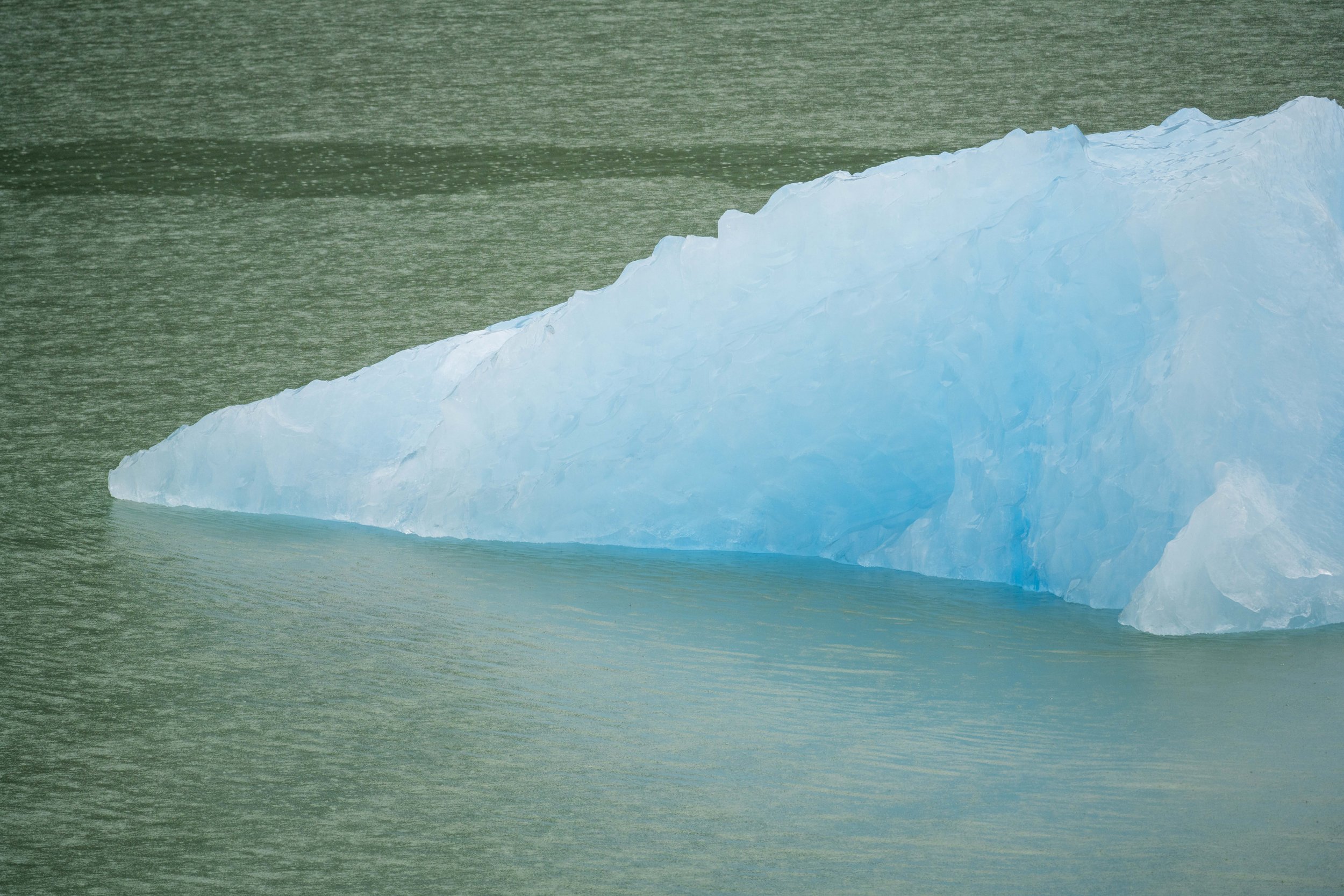 A glowing blue iceberg in greenish water.