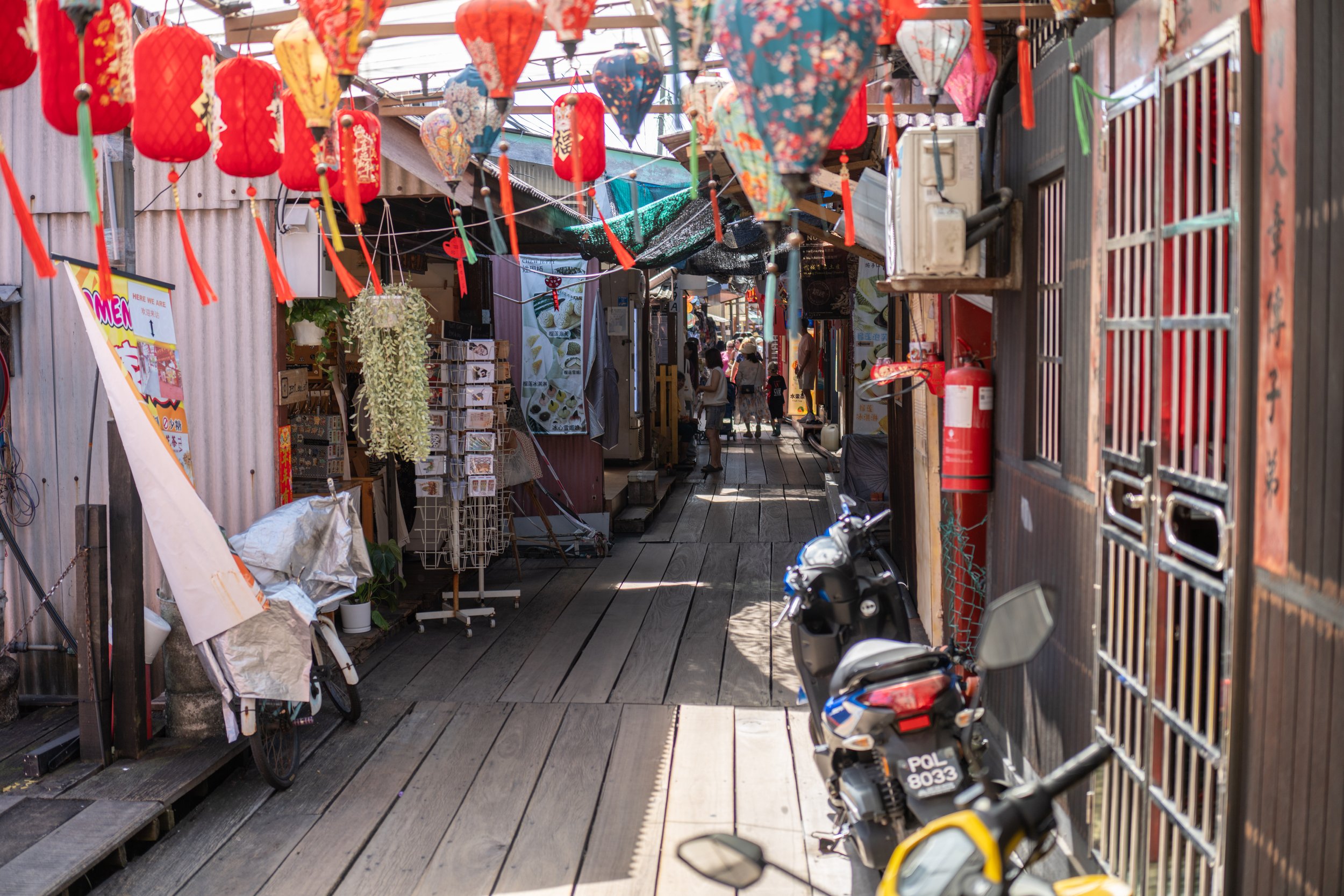 A boardwalk with shops on both sides and lanterns hanging overhead.