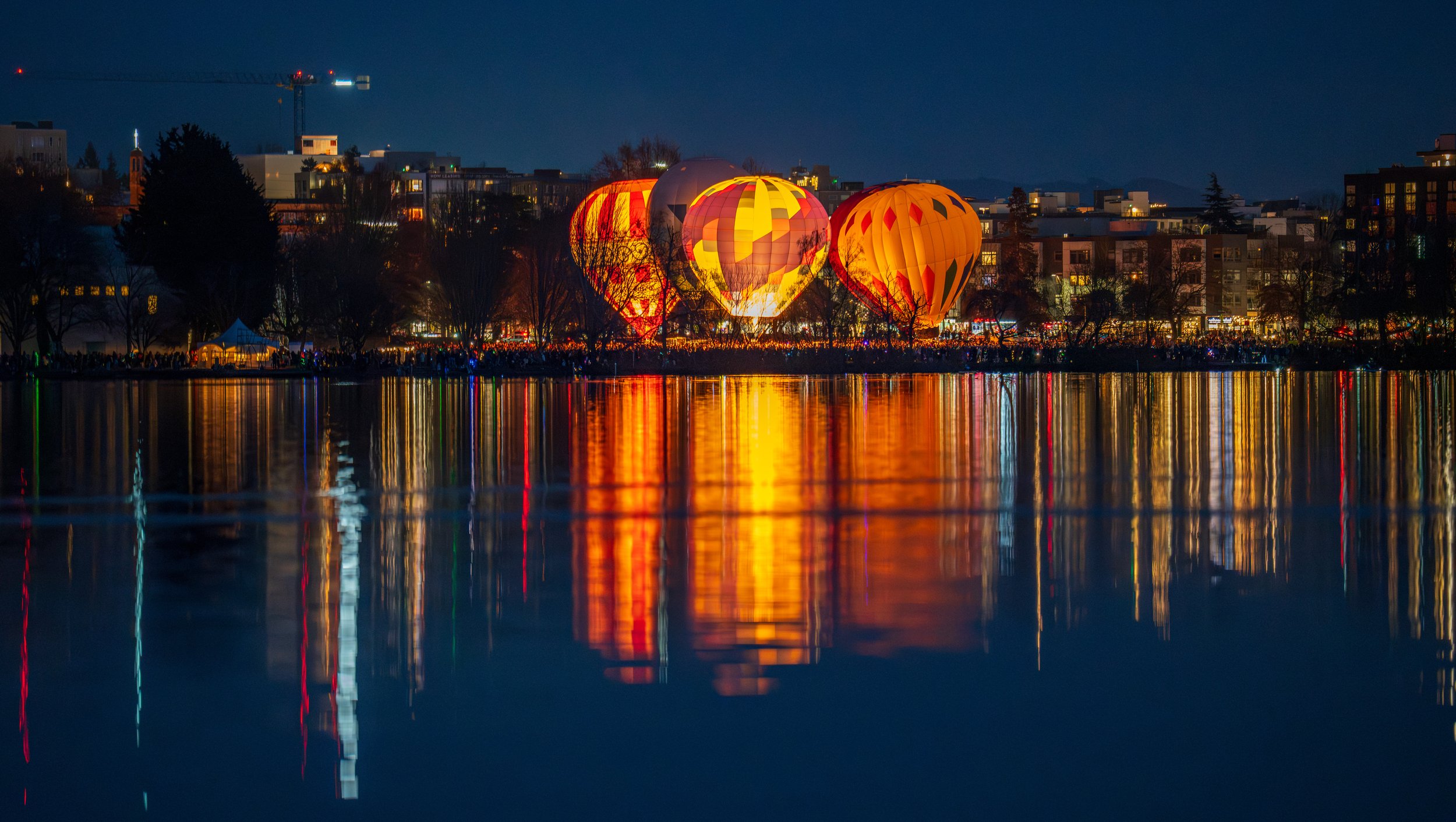 Looking out over a dark lake at five lit up hot air balloons.