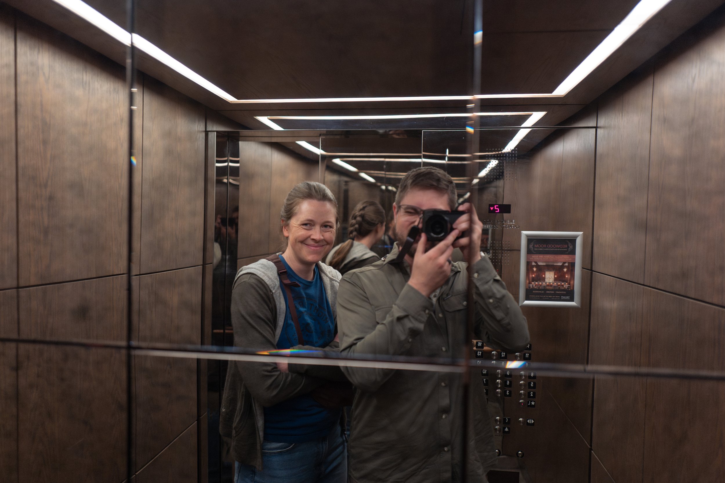 Jason taking a selfie of himself and Nicole in an elevator mirror.