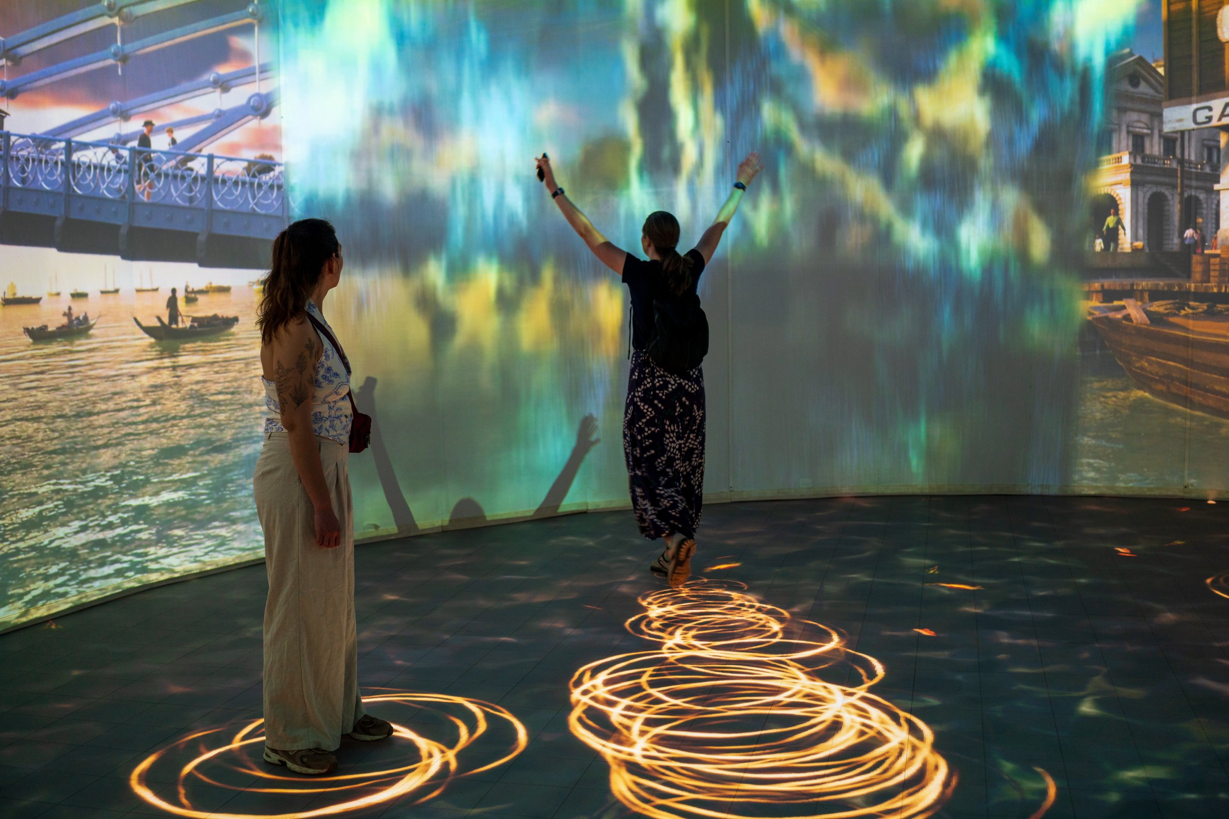 Nicole walking toward a wall and raising her arms to modify the background while Bella watches.