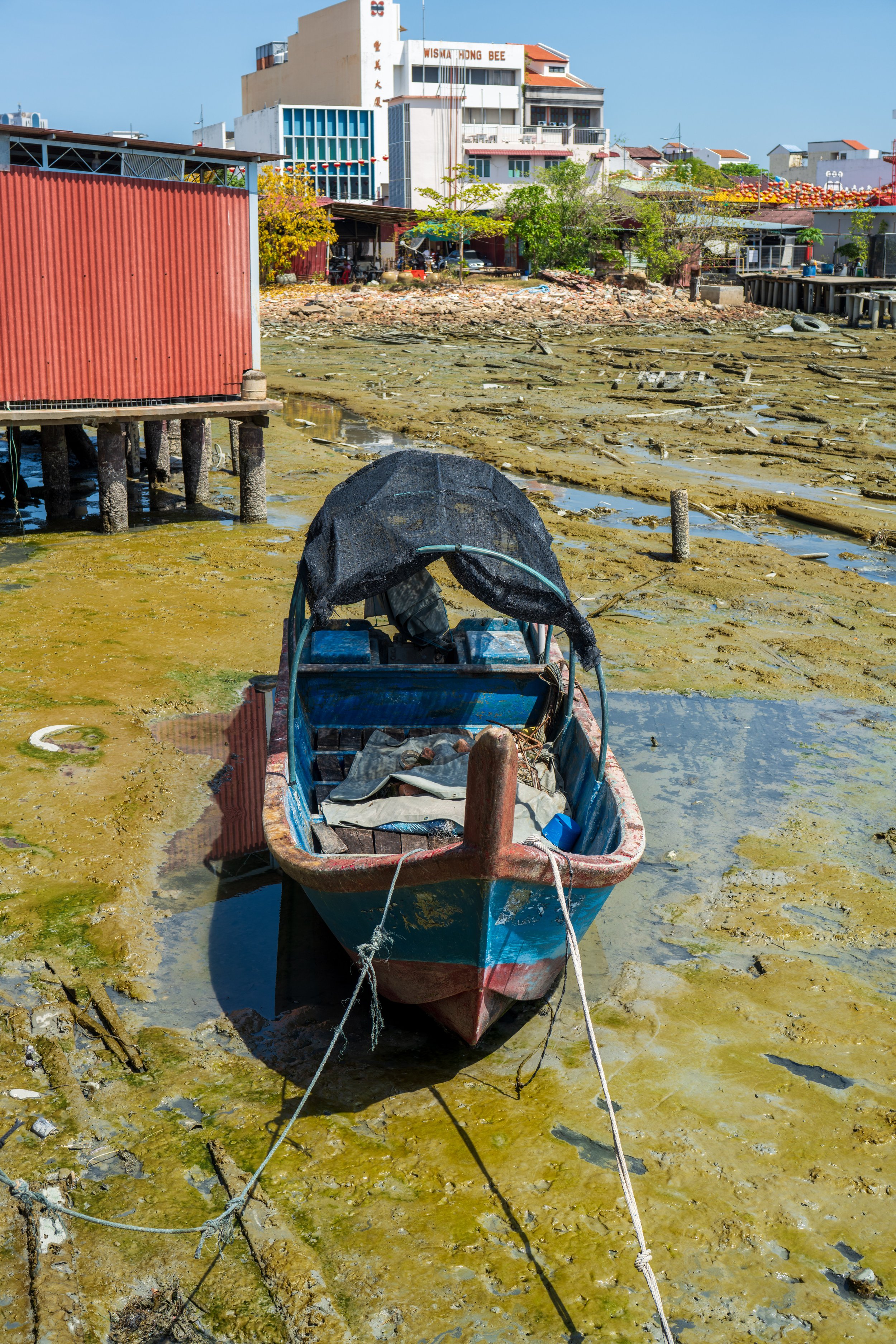 A small boat sitting in greenish tidal mud.