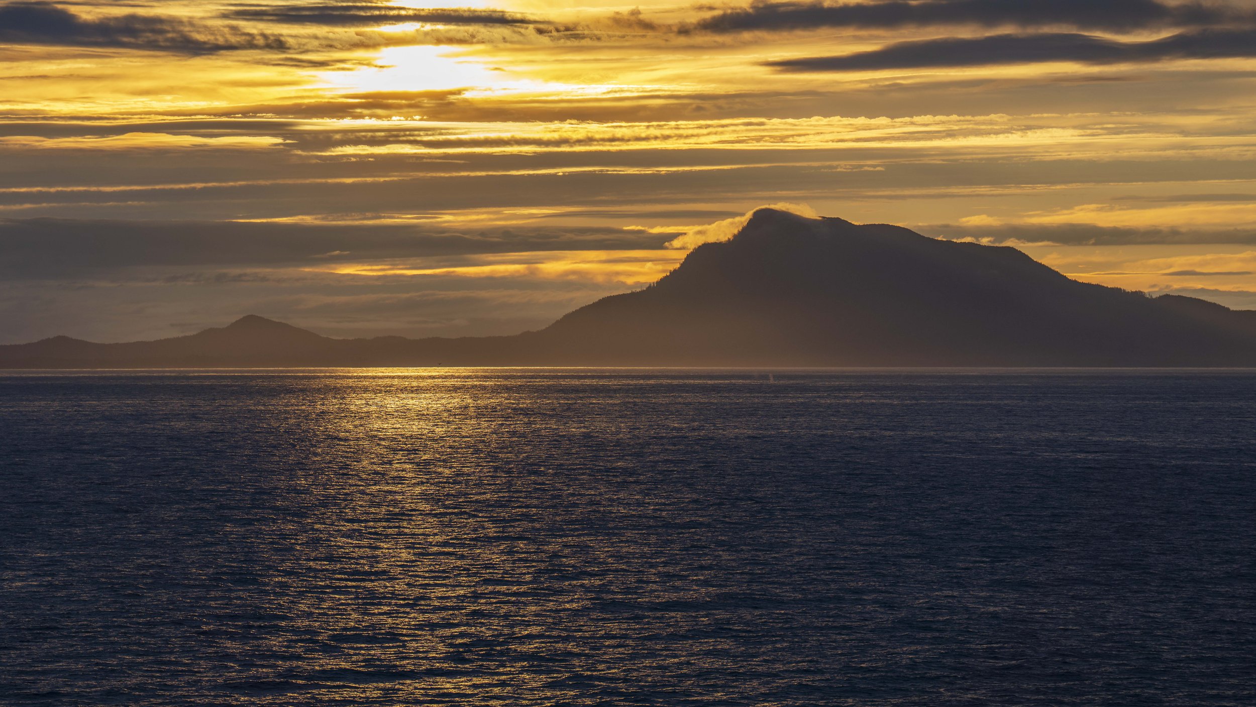 An ocean with mountains and an orange sunrise in the background.