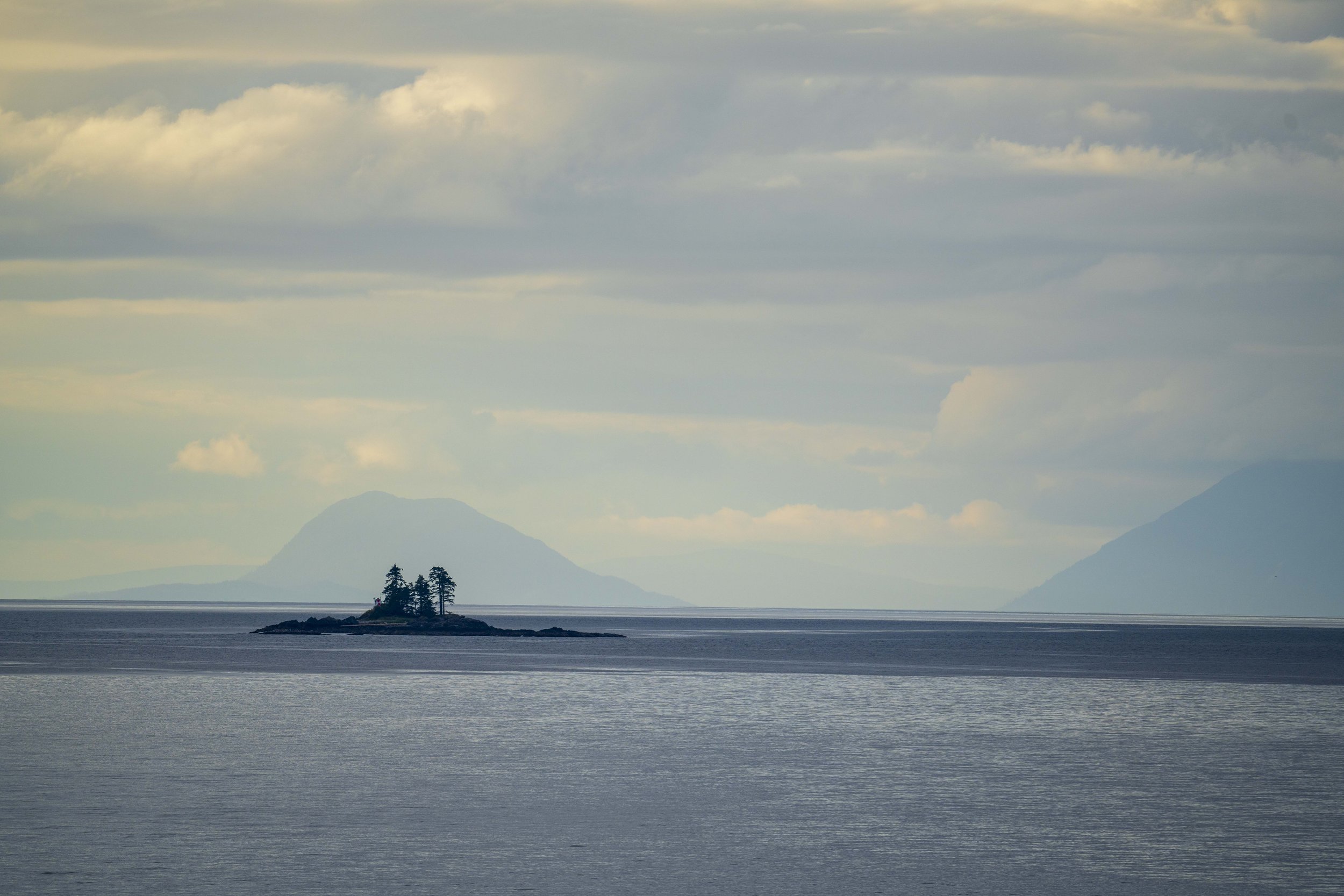 A small island in the ocean with a mountain in the background.