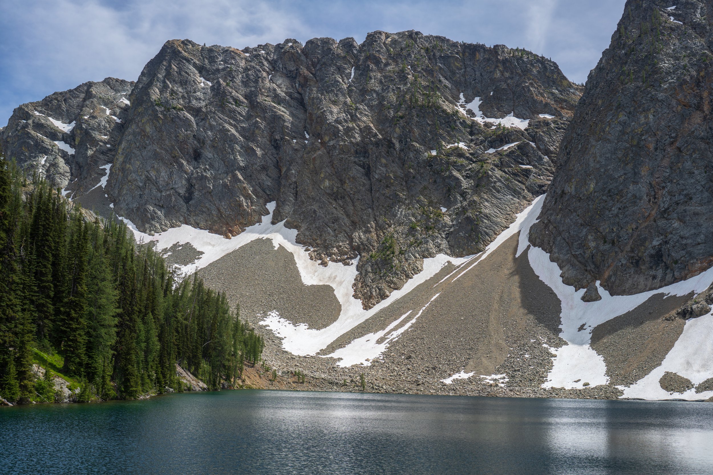 Looking across a lake at a mountain face with some snow.