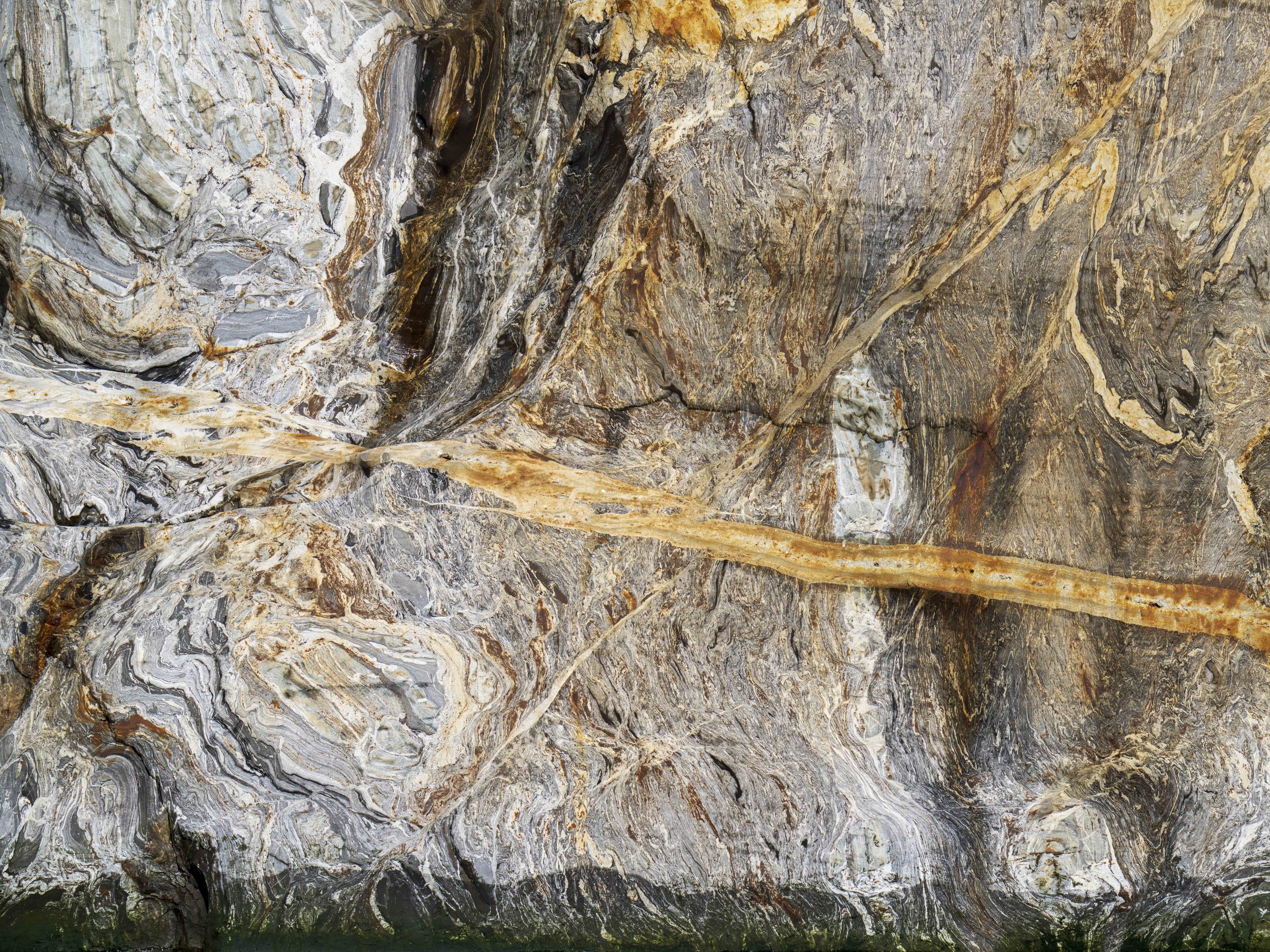 A multilayered gray and orange rock wall.