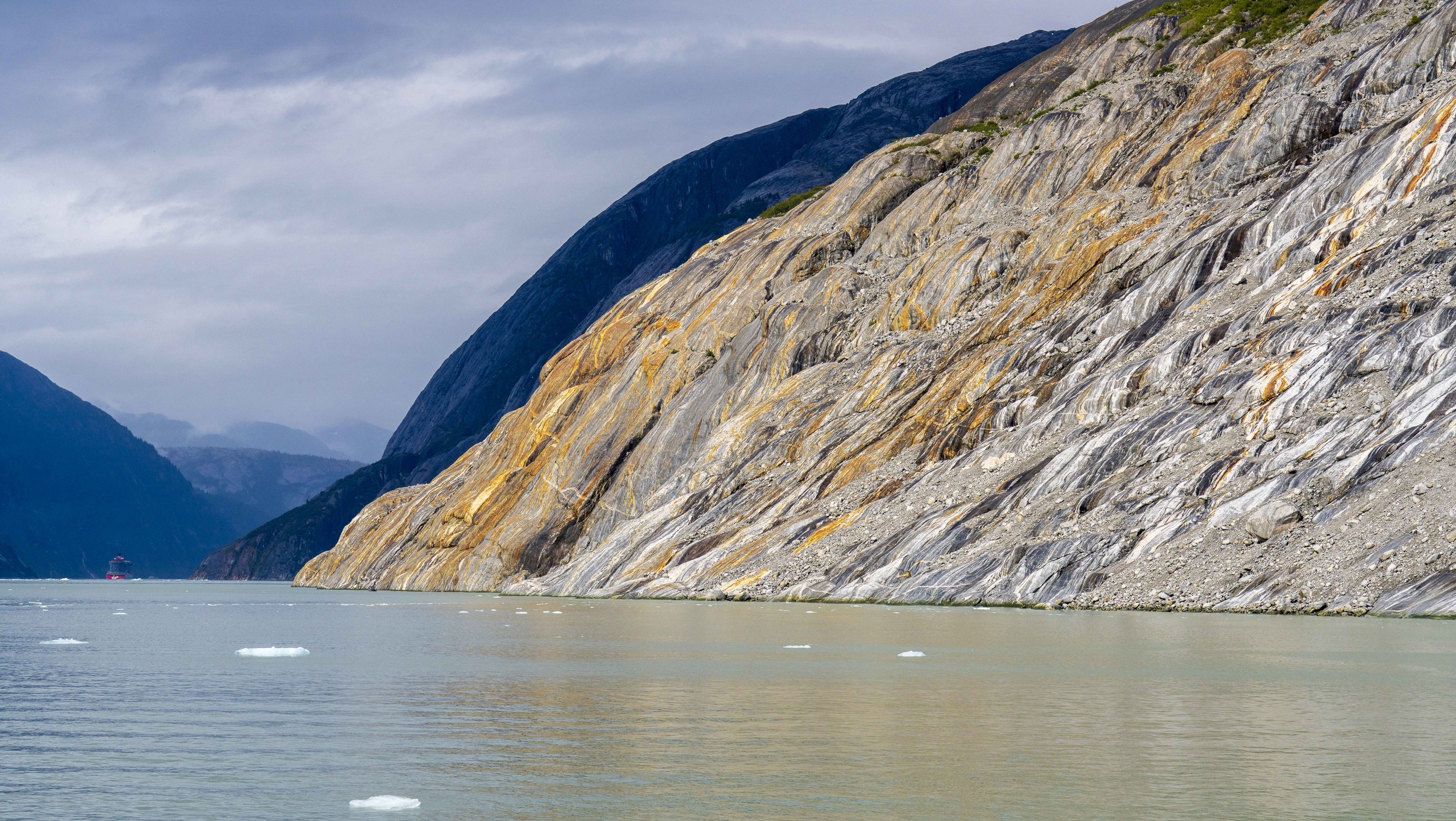 A cruise ship barely visible between mountains on either side of the water.