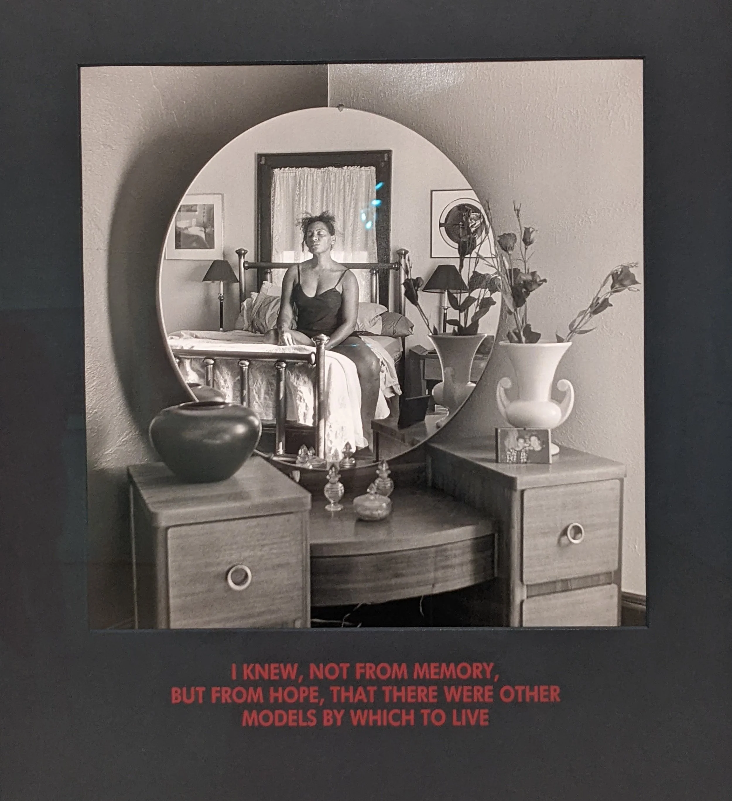 An art piece called Not Manet’s Type (1997) by Carrie Mae Weems that depicts a women's reflection in the mirror—she's sitting on a bed with her eyes closed.