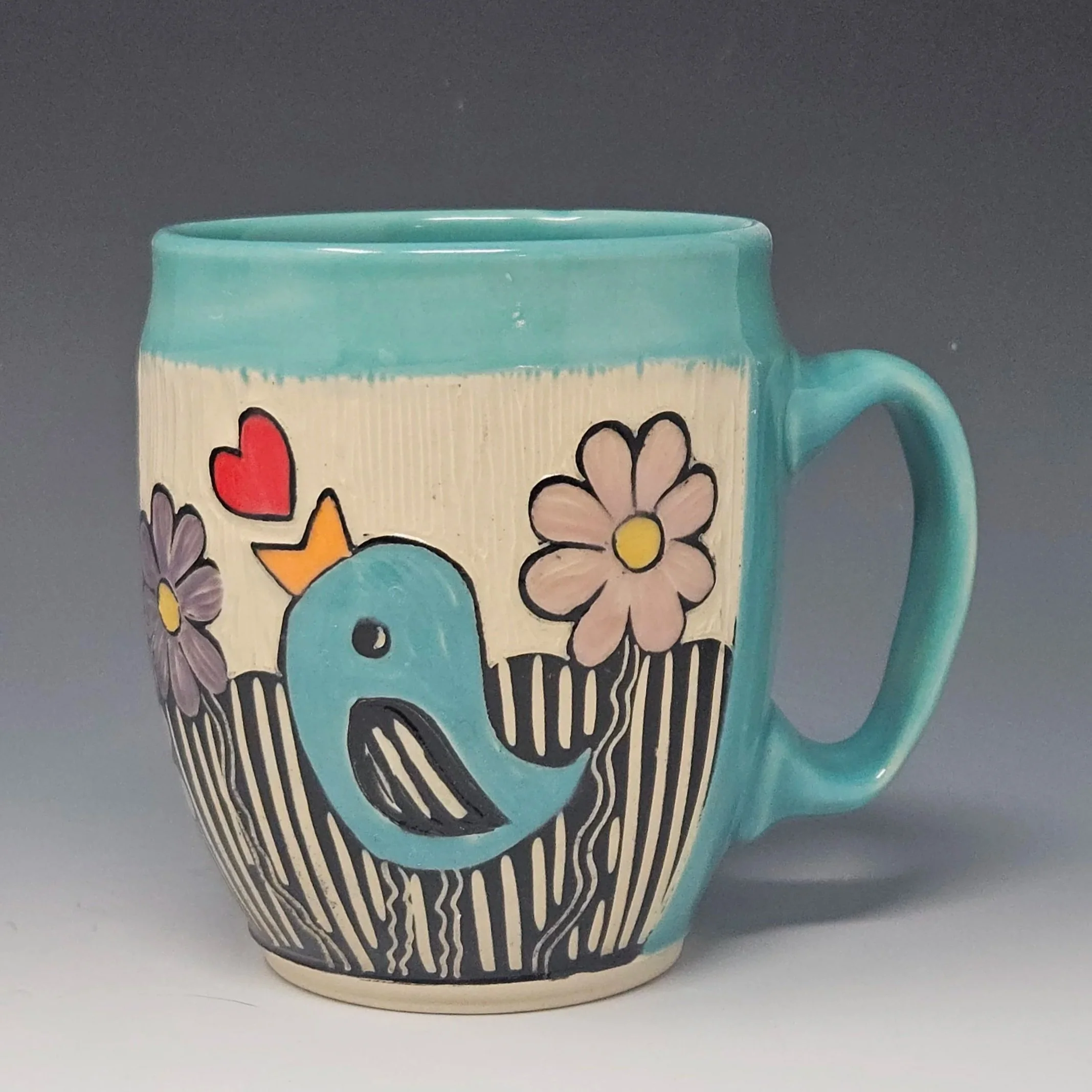 This handmade mug features a little bird and flowers design. This wheel-thrown ceramic art mug has a sgraffito design hand carved on the surface.