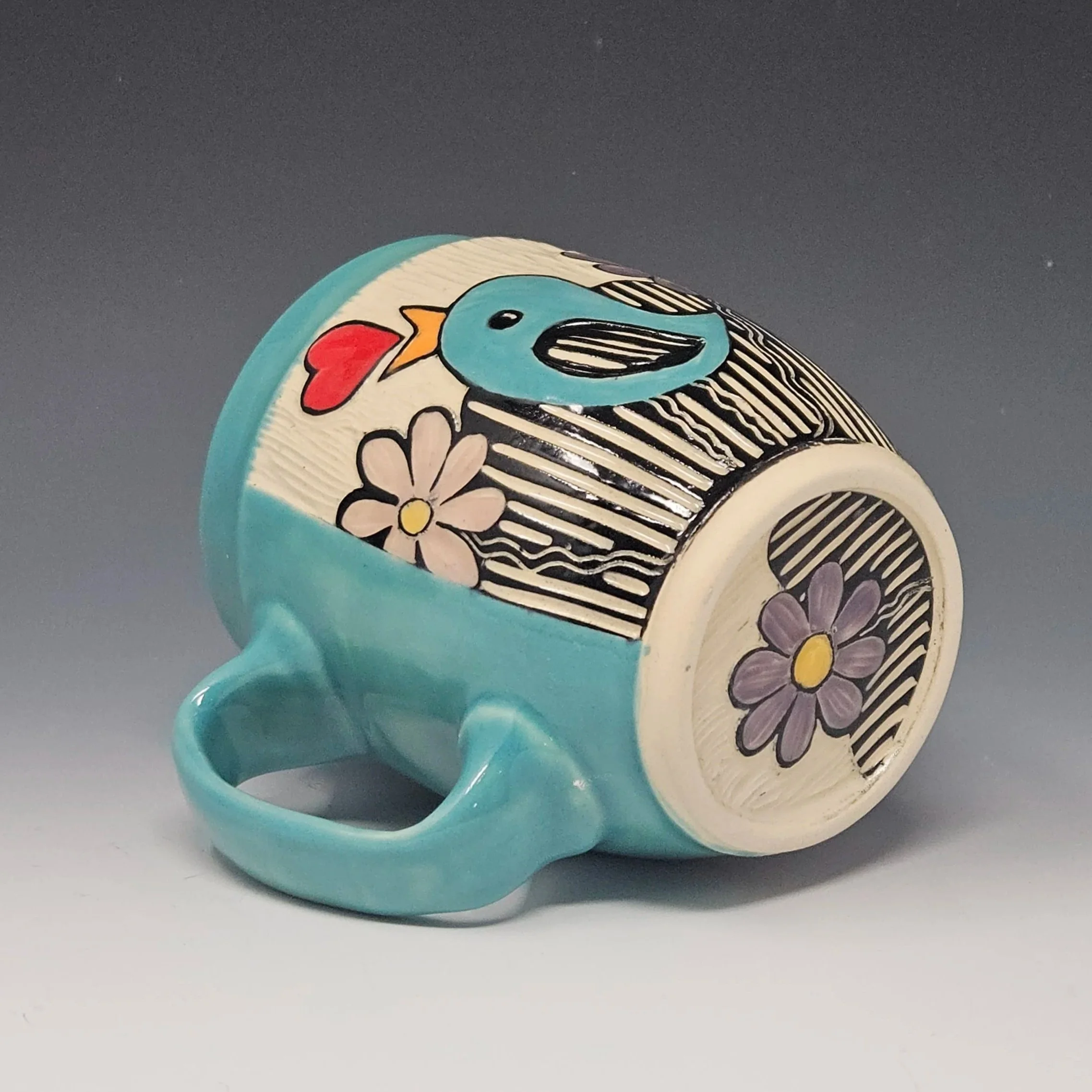 This handmade mug features a little bird and flowers design. This wheel-thrown ceramic art mug has a sgraffito design hand carved on the surface