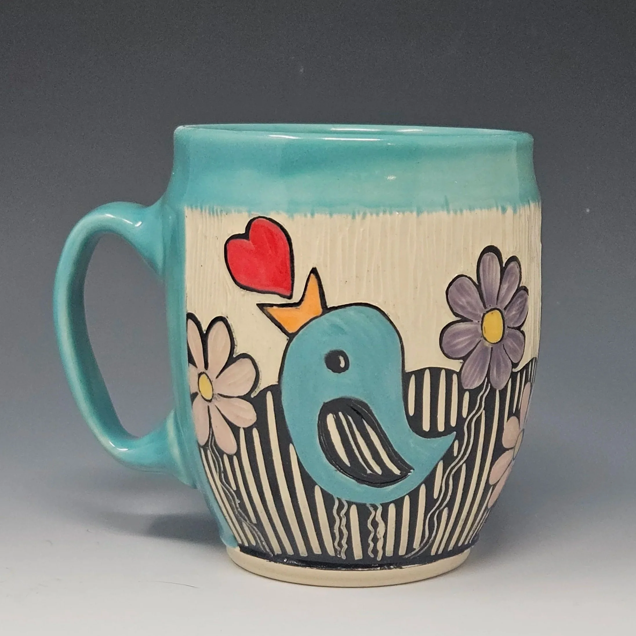 This handmade mug features a little bird and flowers design. This wheel-thrown ceramic art mug has a sgraffito design hand carved on the surface.