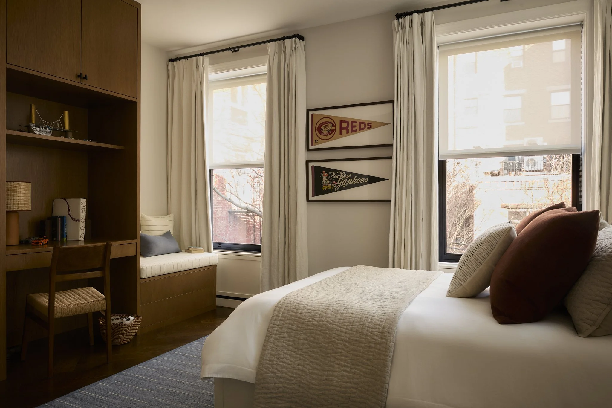 Boy's bedroom with framed vintage baseball pennants, a built-in desk and window seat, and rust and cream bedding
