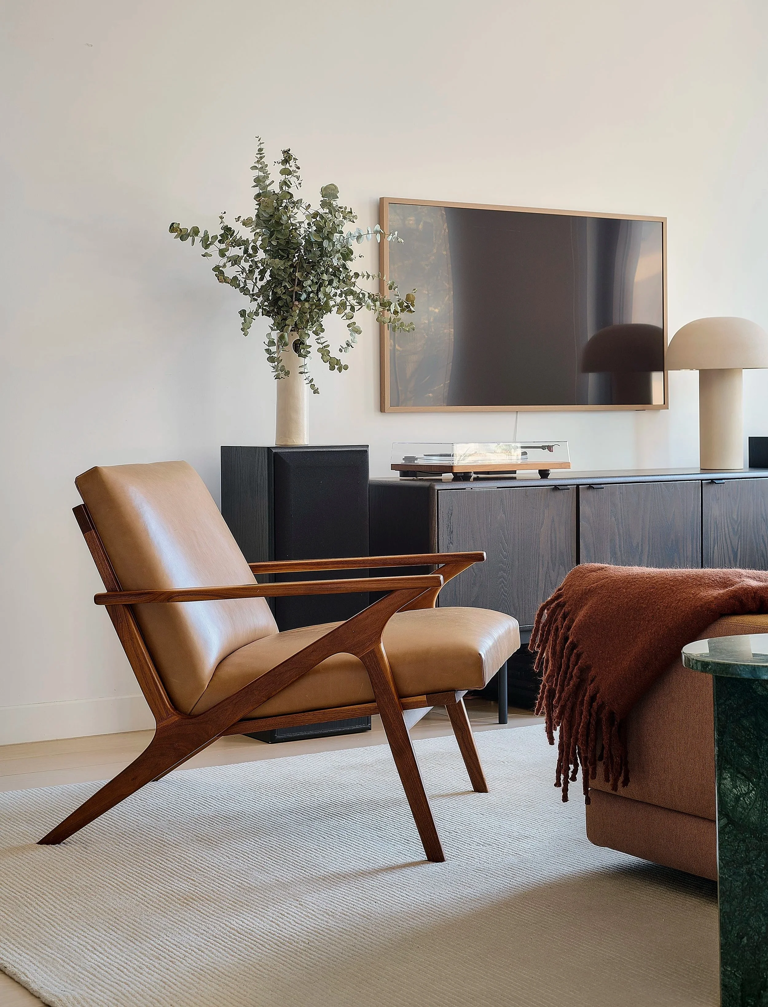 Prospect Heights living room by Hallie Rose Design featuring a vintage mid-century leather lounge chair, dark wood media console, turntable, sculptural lighting, and green marble side table.
