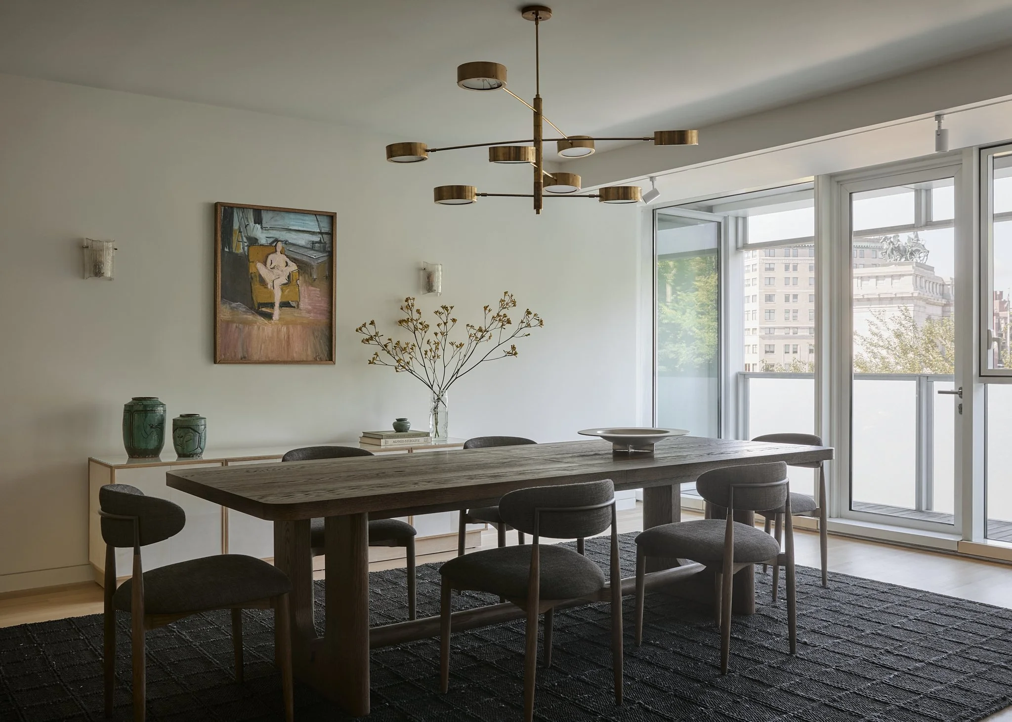 Dining room with a dark oak trestle table, sculptural brass chandelier, and figurative painting in a New York City home