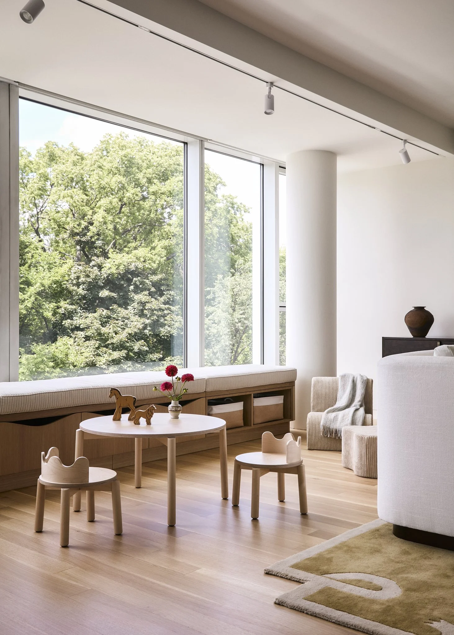 Children's playroom with built-in window seating, round wood play table, and wooden toy horse and lion in a NYC apartment