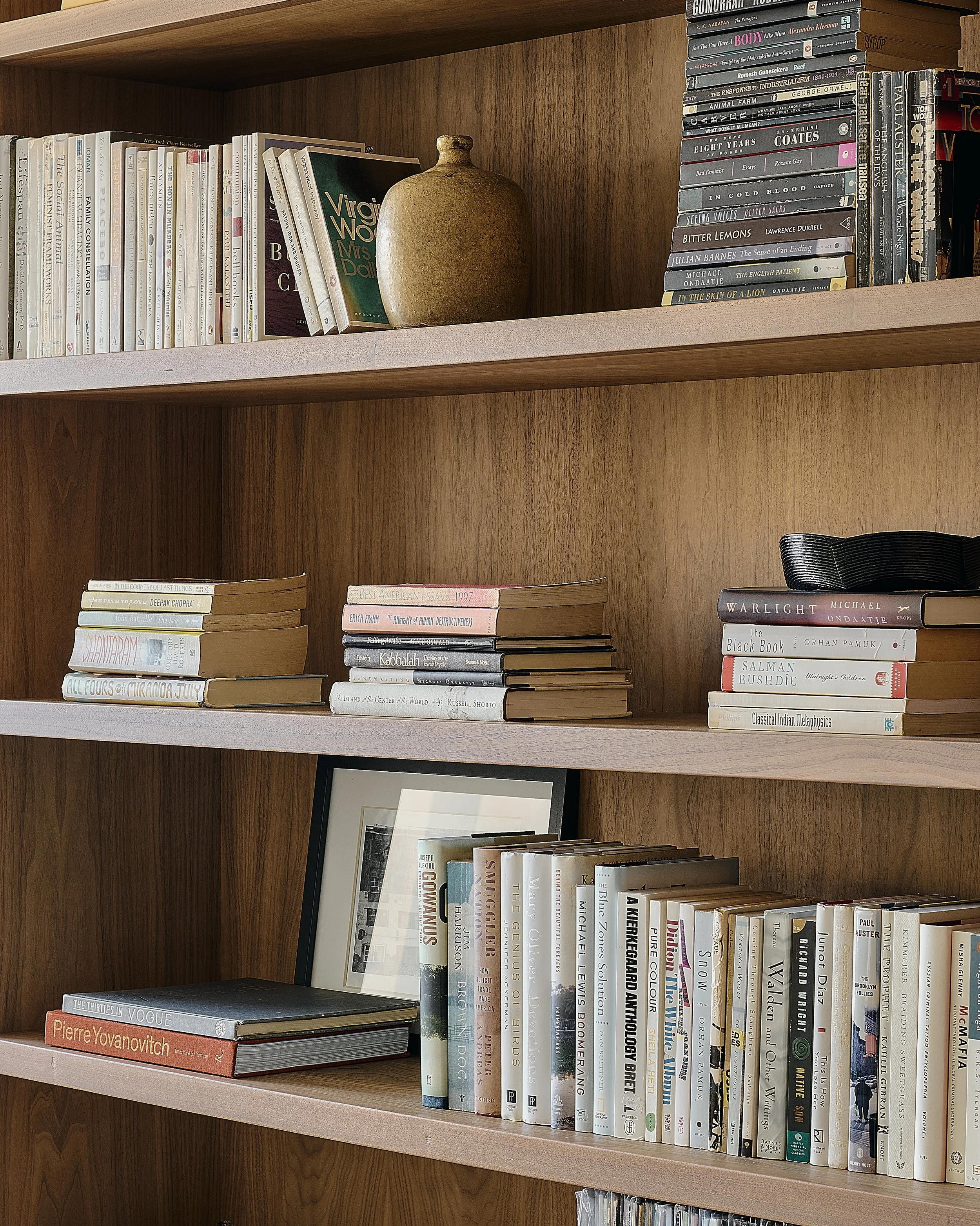 Detail of custom walnut bookshelves in a Prospect Heights apartment by Hallie Rose Design, styled with collected books, a ceramic vessel, framed artwork, and sculptural objects.