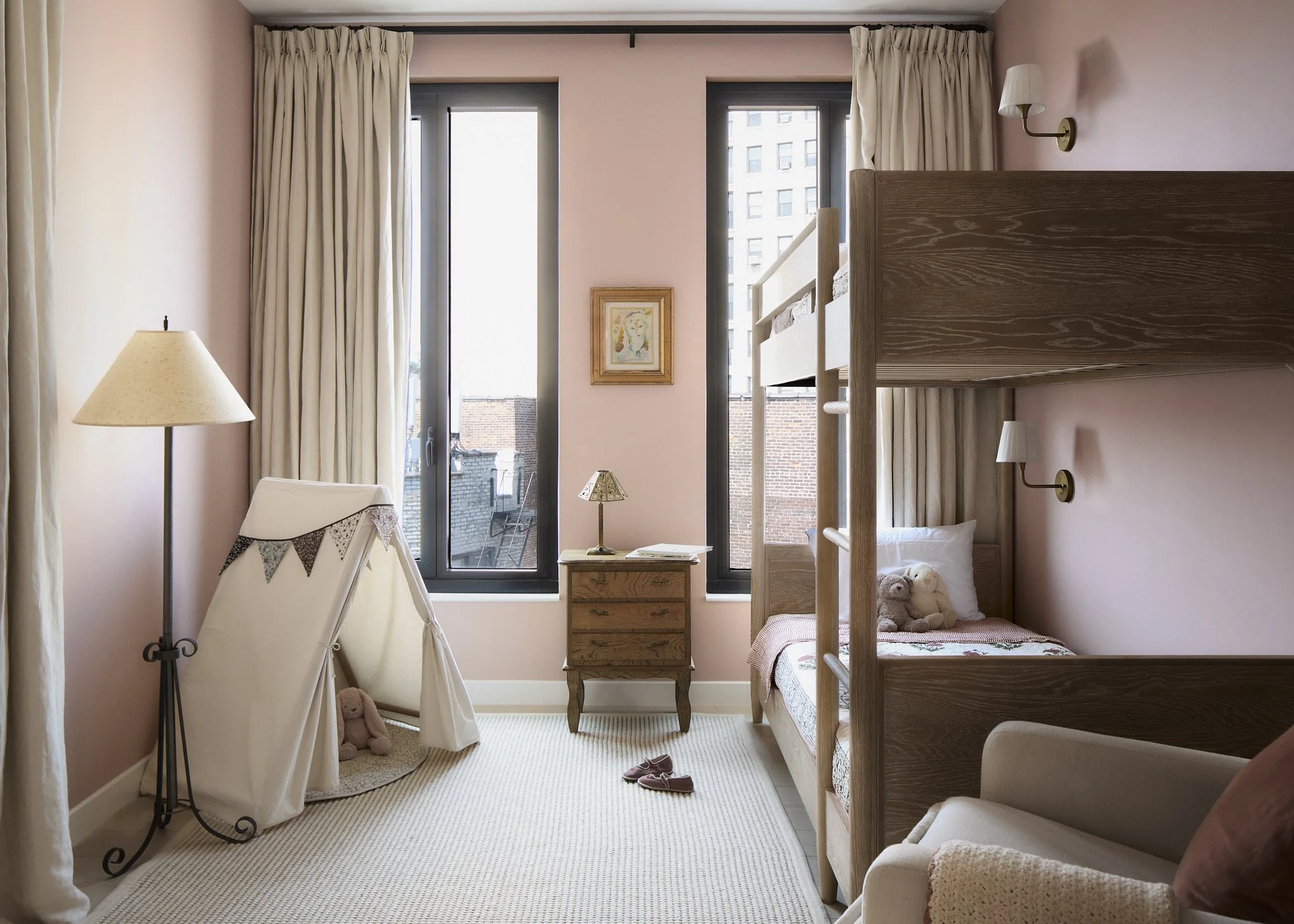 Prospect Heights shared children’s bedroom by Hallie Rose Design featuring oak bunk beds, blush-pink walls, linen curtains, vintage wood dresser, reading sconces, and a canvas play tent.