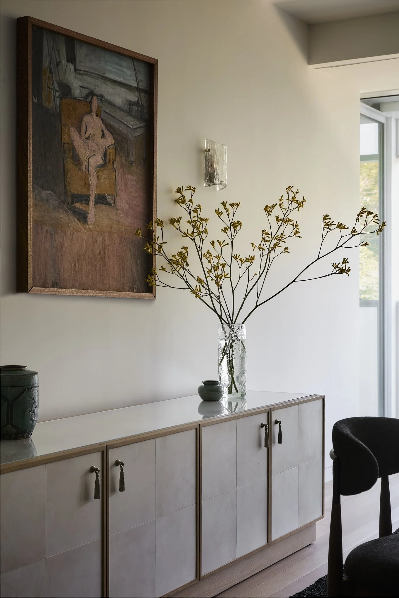 Sideboard styled with a figurative oil painting, glass wall sconce, and ceramic vase in a New York City residential interior