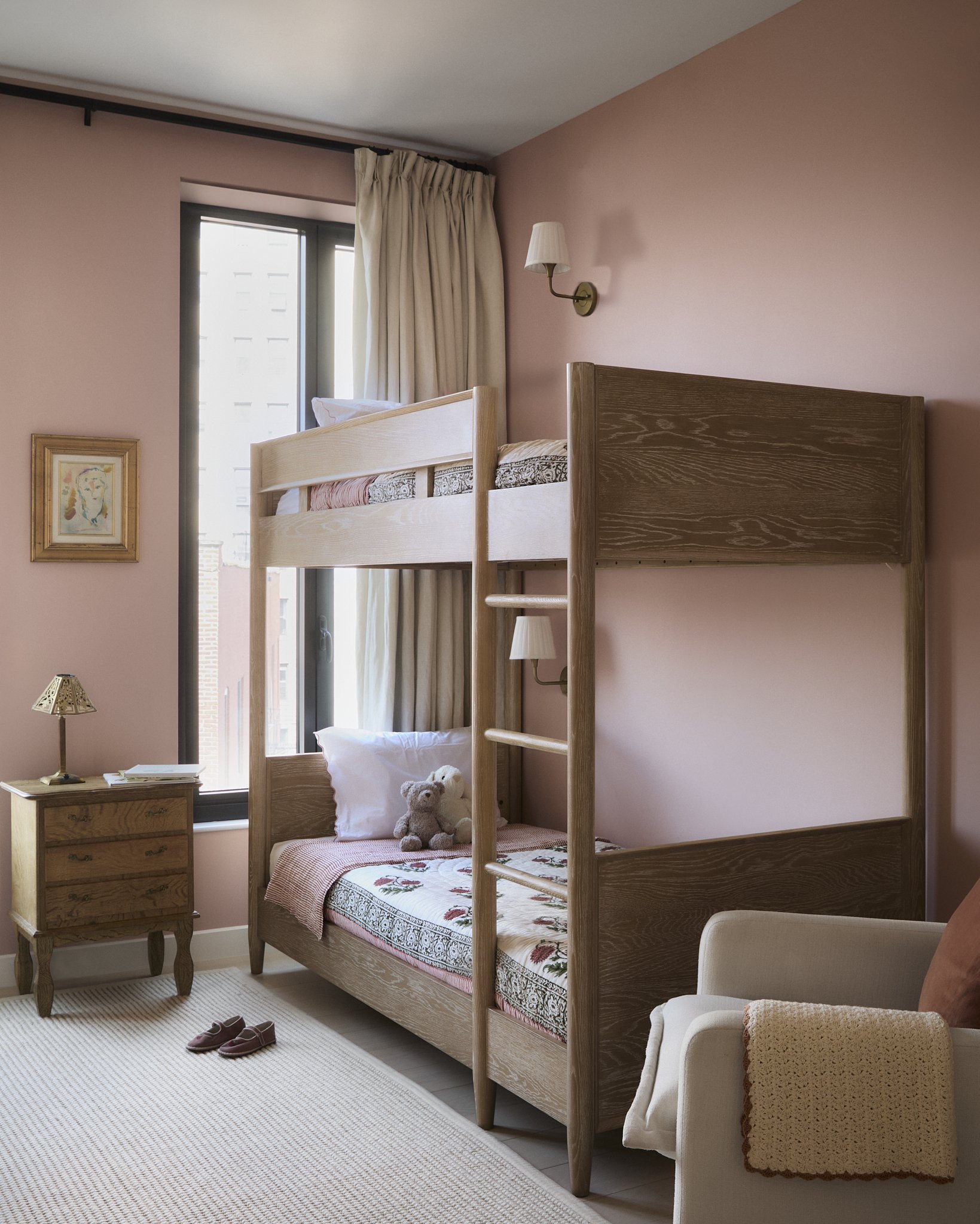 Girl's bedroom with a custom oak bunk bed, blush pink walls, floral block-print bedding, and vintage brass sconces in a New York City apartment