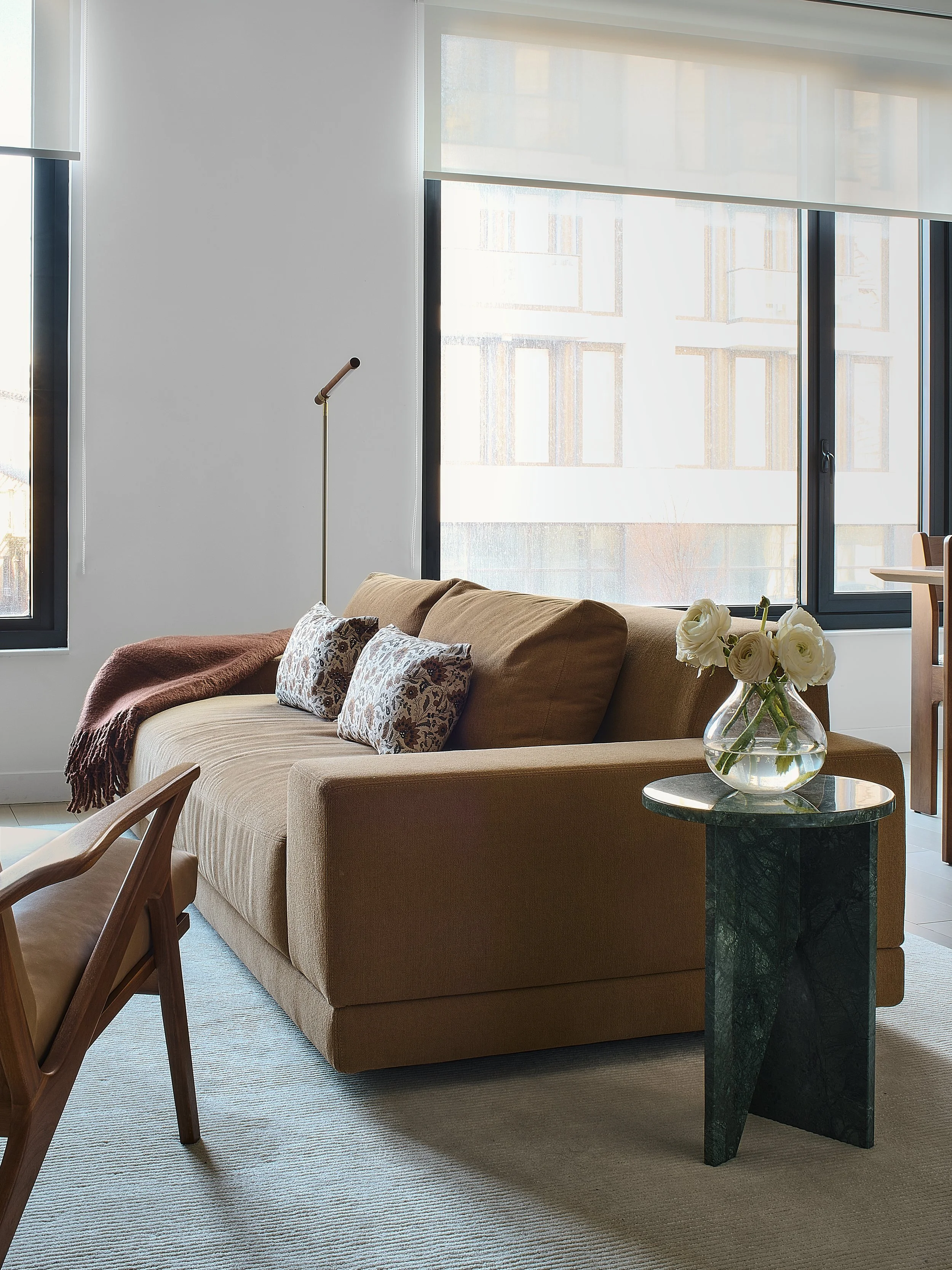 Living room with a camel wool sofa, floral throw pillows, and a green marble side table styled with ranunculus