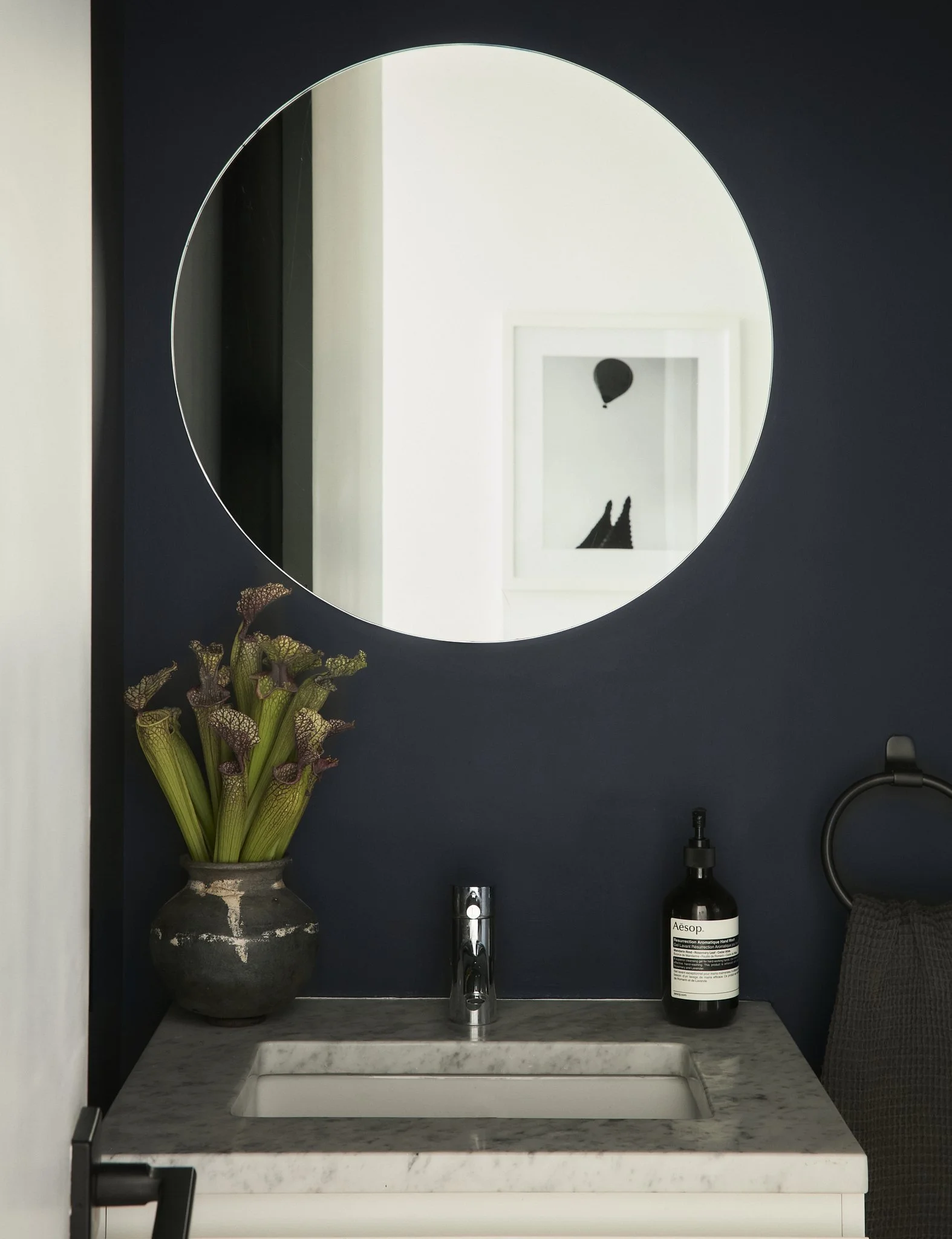 Prospect Heights powder room by Hallie Rose Design featuring deep navy walls, a round frameless mirror, Carrara-style marble vanity, chrome faucet, and collected ceramic vessel.