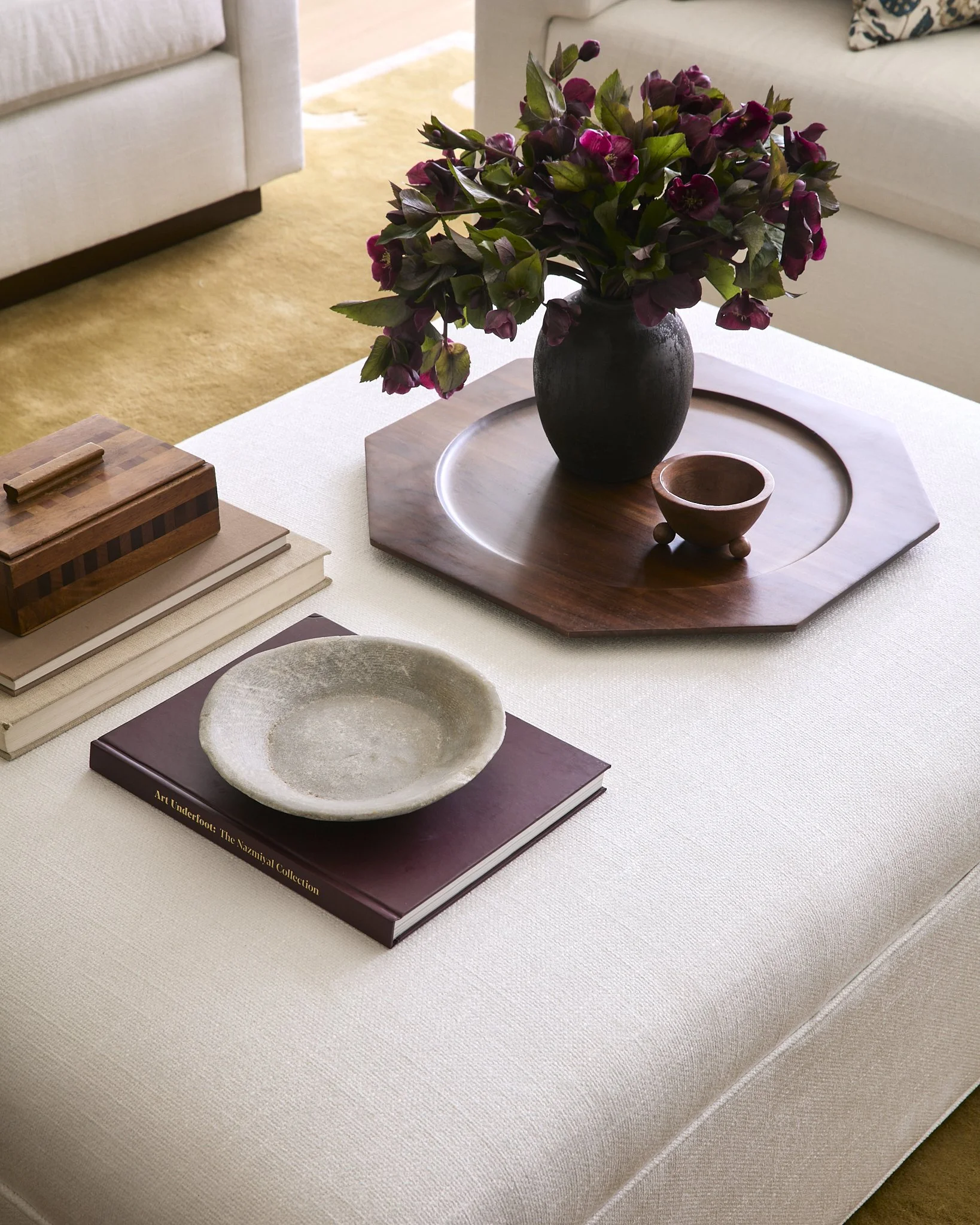 Coffee table styled with an octagonal wood tray, dark ceramic vase of hellebores, and stacked design books
