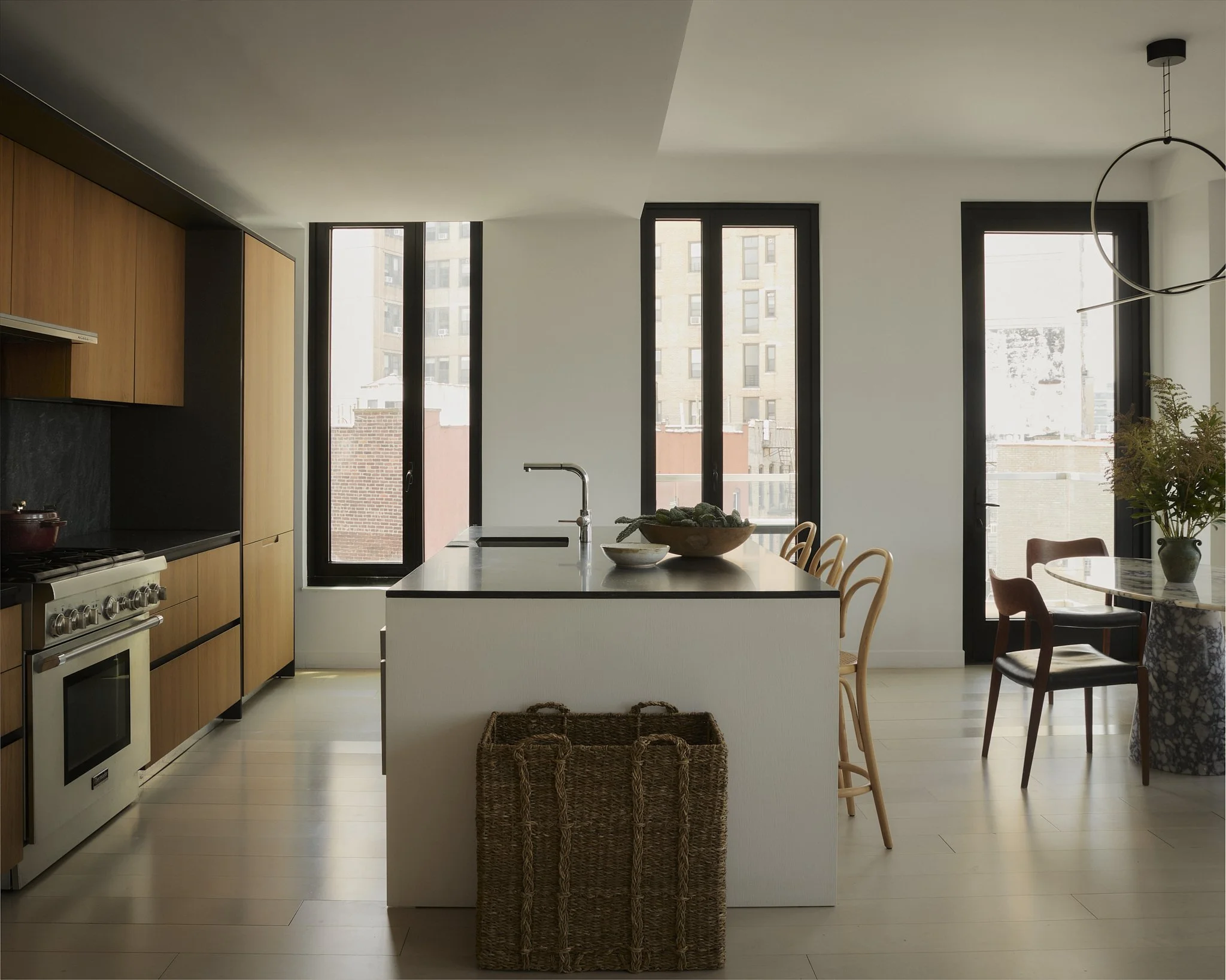 Prospect Heights kitchen by Hallie Rose Design featuring flat-panel walnut cabinetry, integrated appliances, a reeded island with dark stone countertop, bentwood counter stools, and black-framed windows.