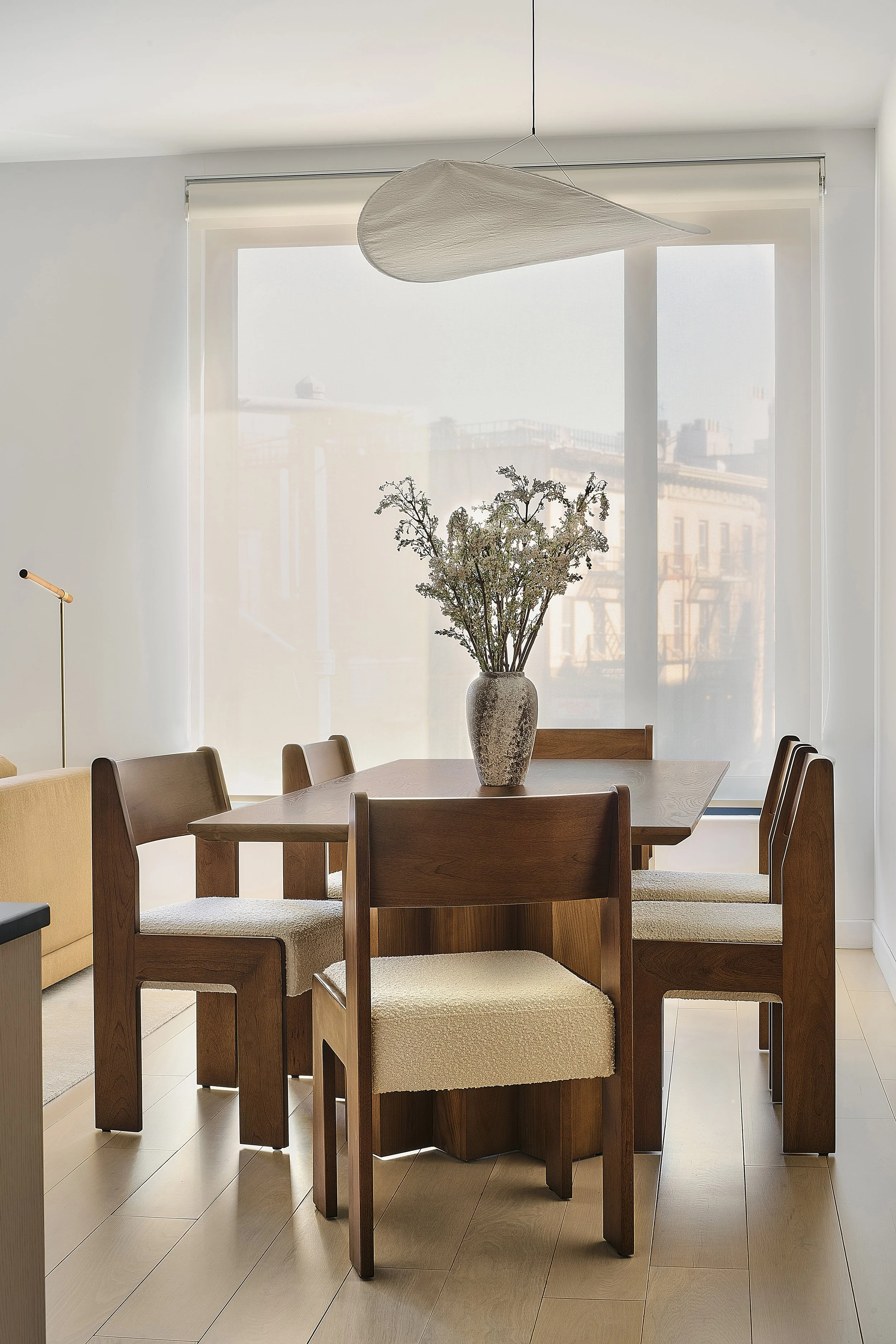 Prospect Heights dining room by Hallie Rose Design featuring a sculptural wood dining table and chairs, textured upholstery, an oversized paper pendant light, and a vintage ceramic vase.