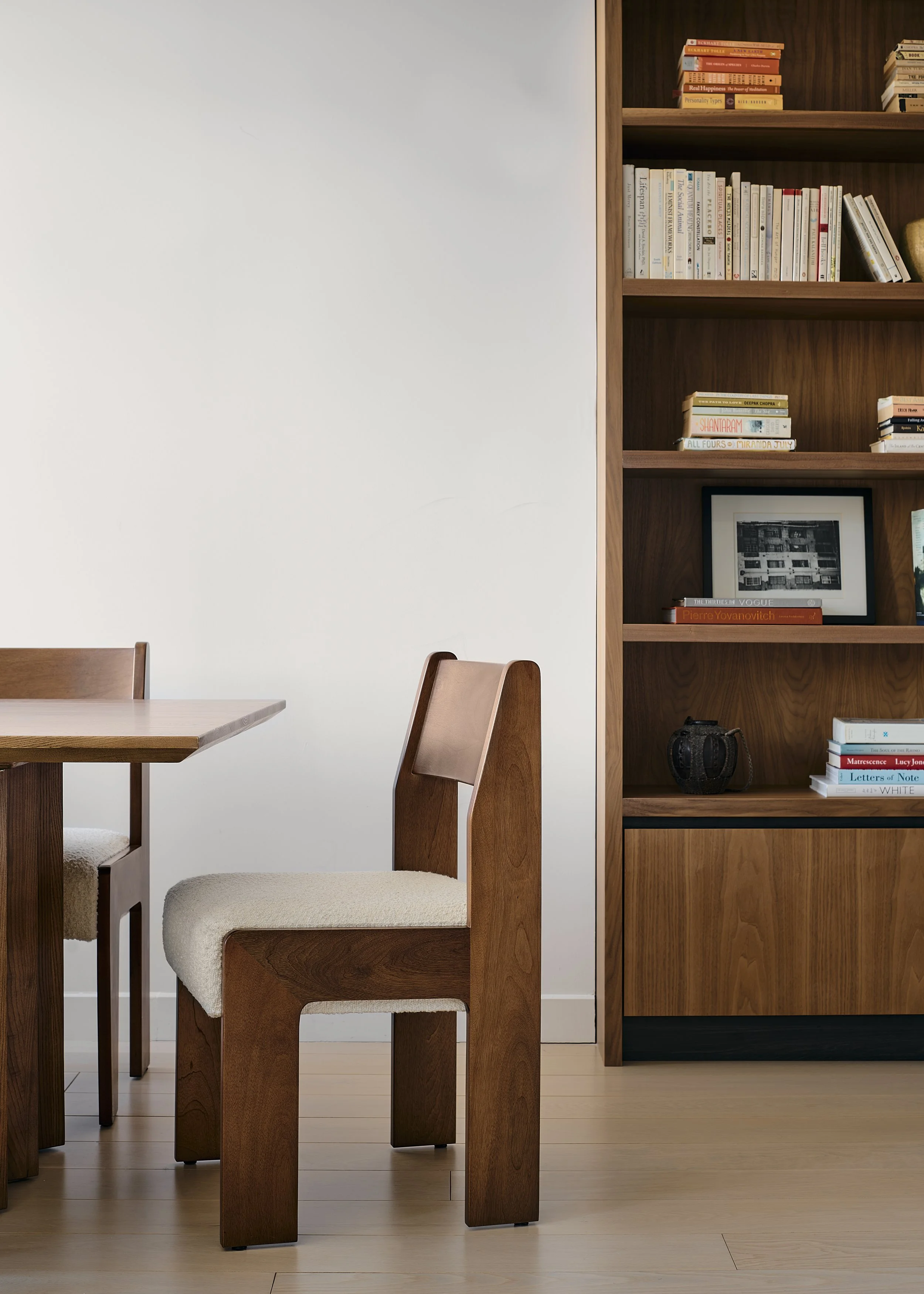 Prospect Heights dining room by Hallie Rose Design featuring custom walnut bookshelves, a sculptural solid-wood dining table, bouclé-upholstered chairs, curated books, and framed artwork.