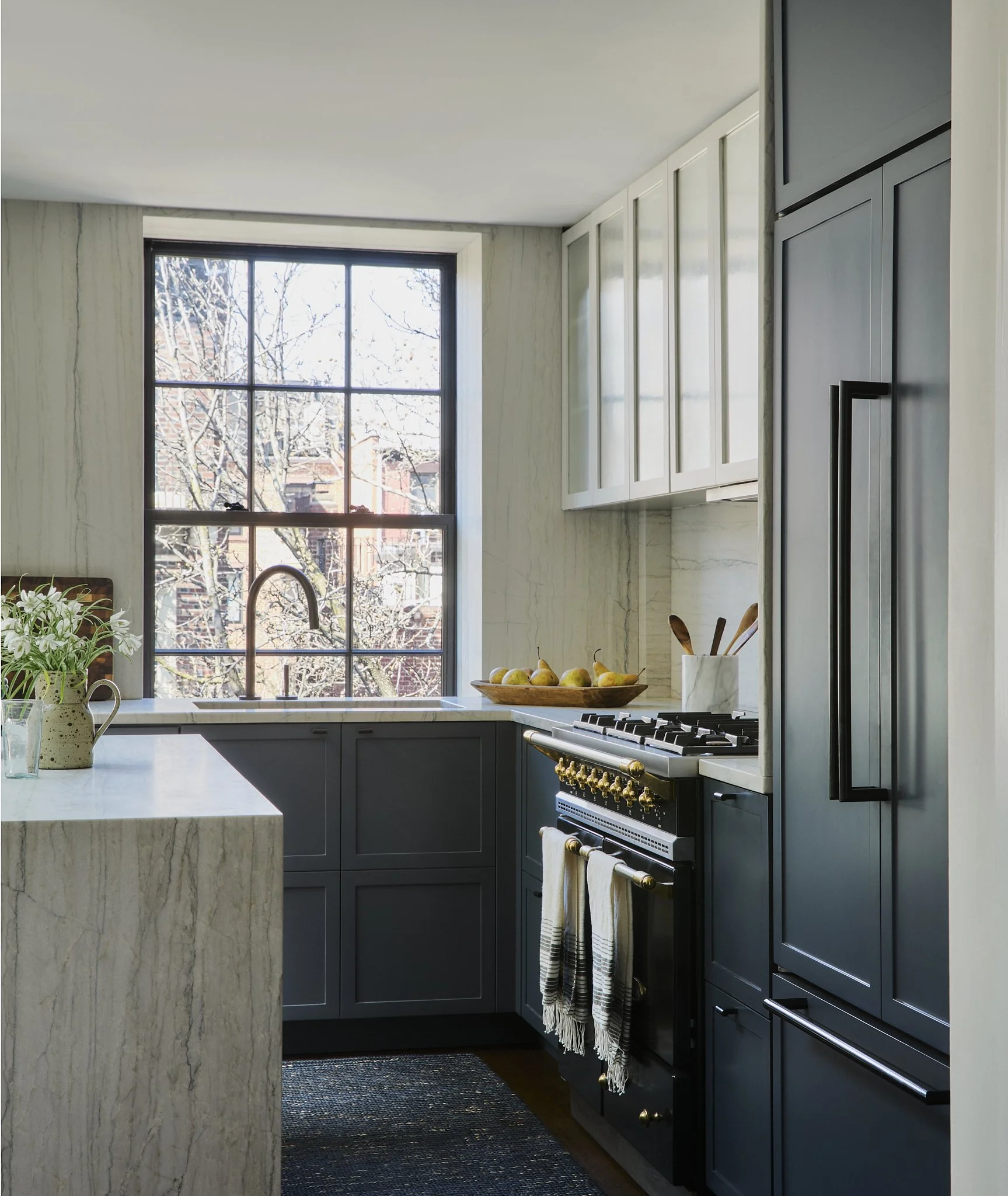 Brooklyn Heights kitchen by Hallie Rose Design featuring dark Shaker cabinetry, White Macaubas-style quartzite surfaces, a waterfall-edge island, black French-style range, and integrated panel-ready refrigerator.