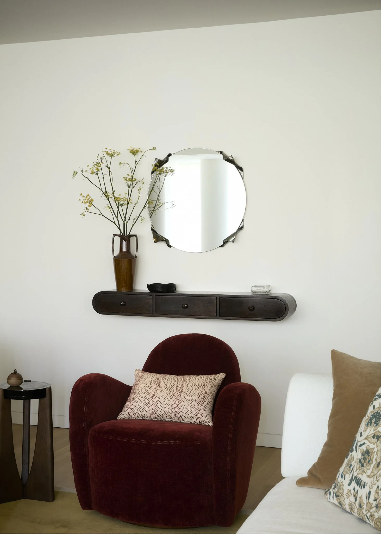 Entryway console table with a round decorative mirror, ceramic vase, and burgundy velvet swivel chair in an NYC apartment