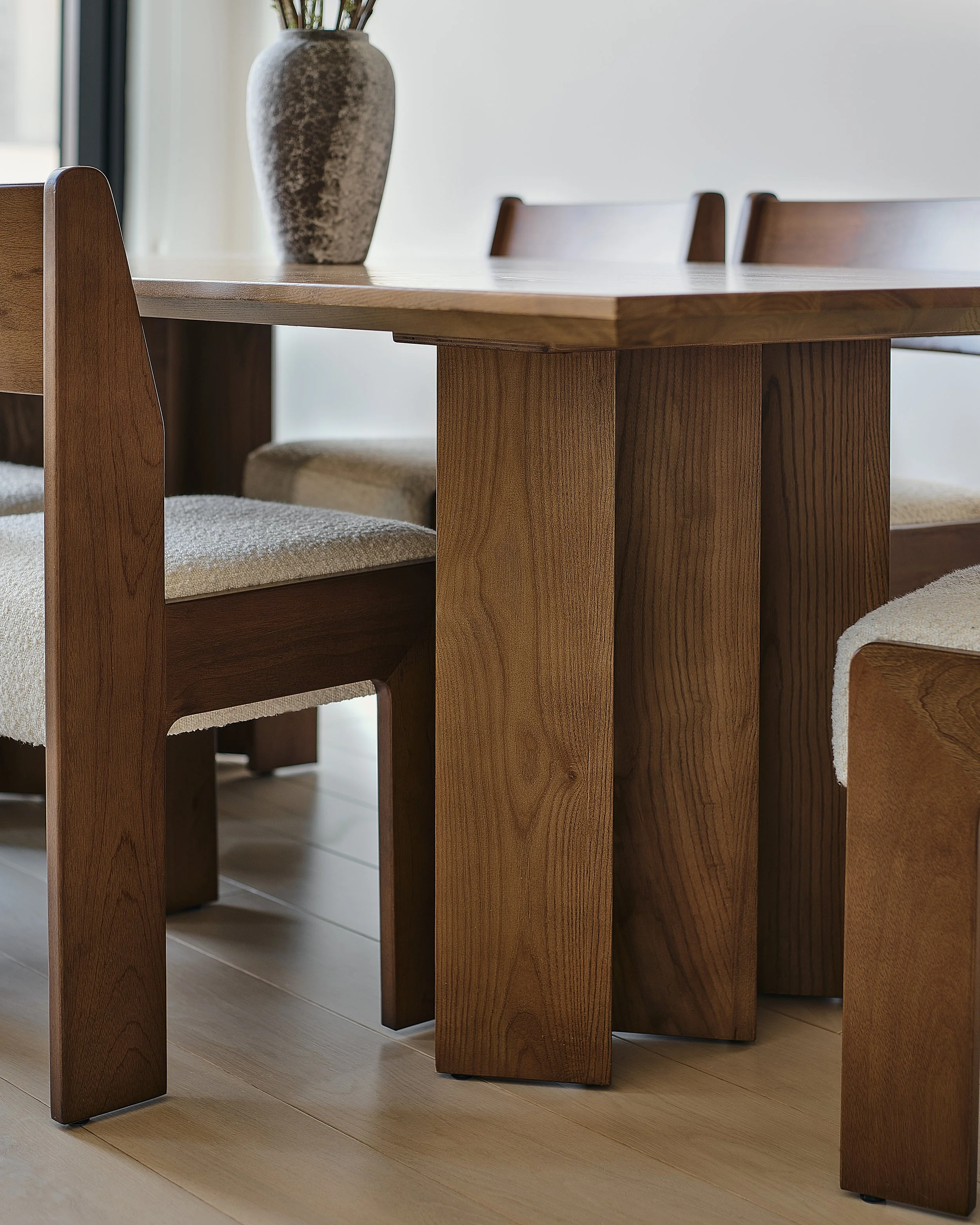 Close-up of a Prospect Heights dining room by Hallie Rose Design featuring a sculptural solid-wood table, architectural dining chairs, textured bouclé upholstery, and ceramic vessel.