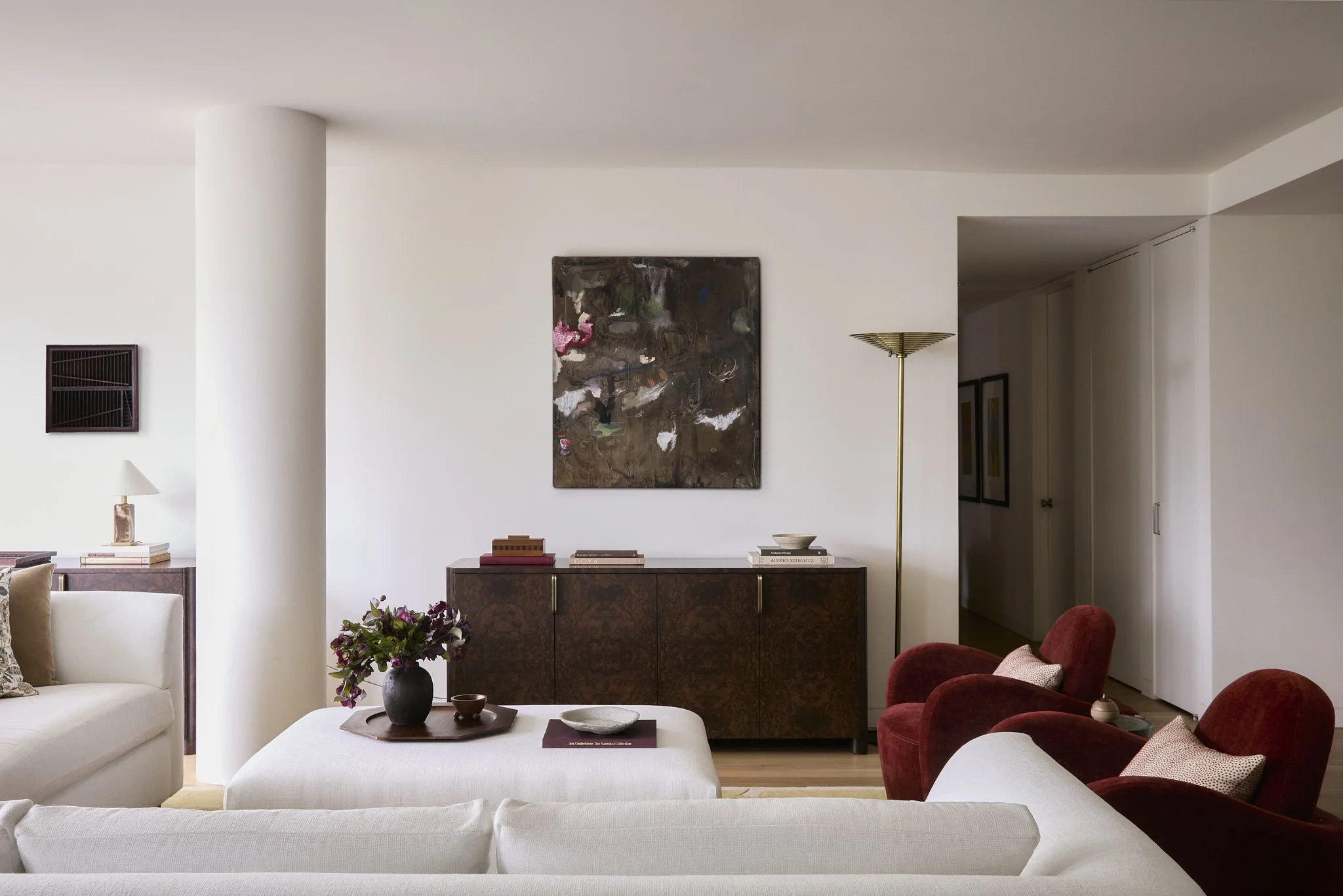 Living room with a burl wood credenza, abstract painting, brass floor lamp, and red velvet chairs in a New York City residence