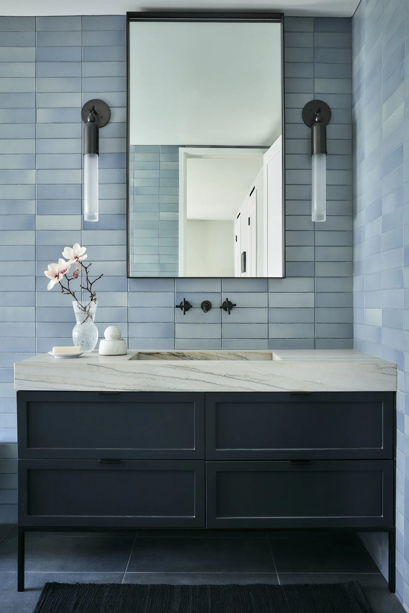 Brooklyn Heights bathroom by Hallie Rose Design featuring a dark floating vanity, integrated stone sink, blue ceramic glazed tile in a horizontal stacked pattern, and black glass sconces.