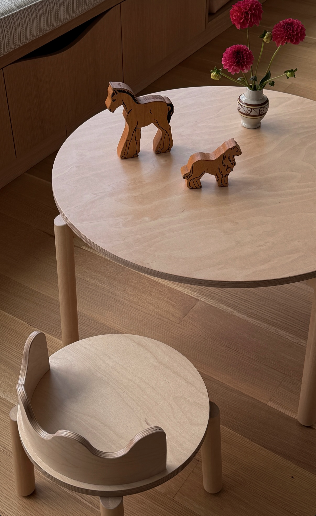 Children’s play area designed by Hallie Rose Design, featuring a round wood table, scalloped chair, handcrafted animal toys, and a small vase of pink flowers.