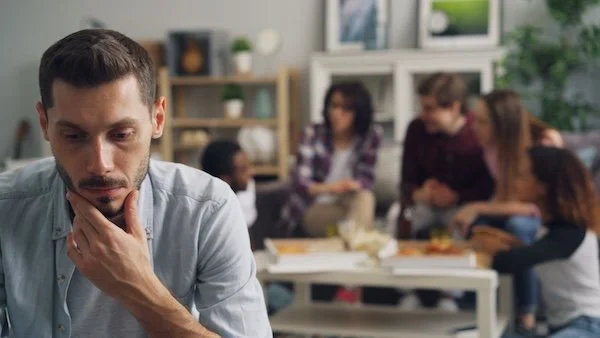 A man alone thinking with friends behind him