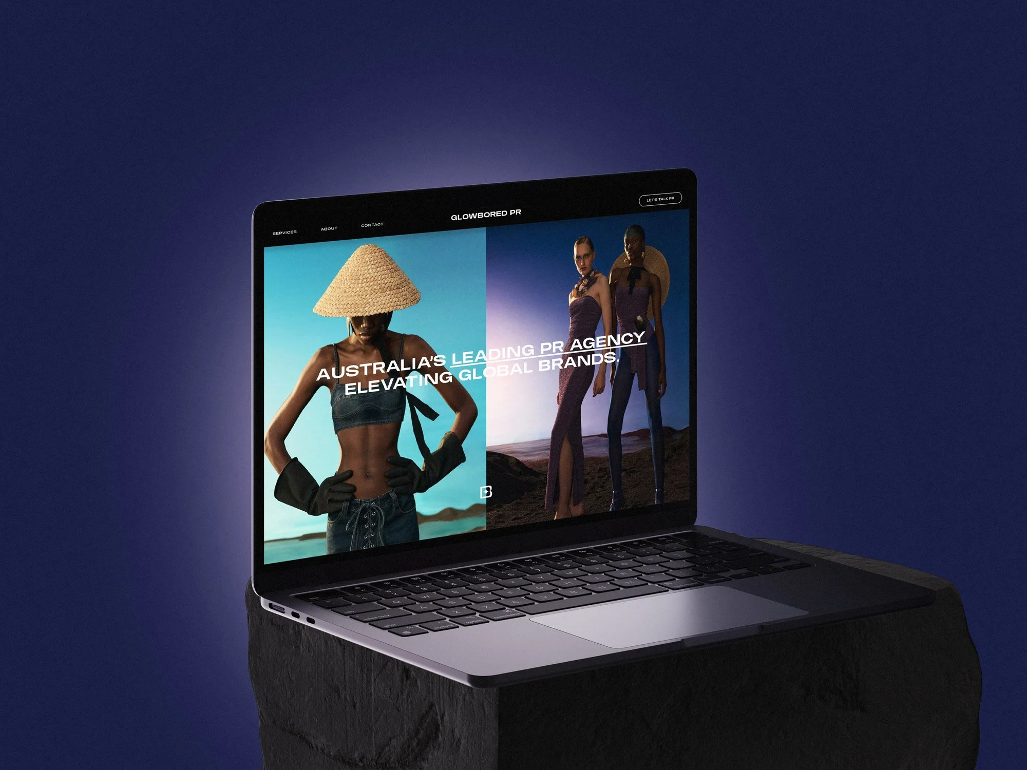 A laptop on a dark surface displaying a fashion website with models wearing stylish clothing and accessories