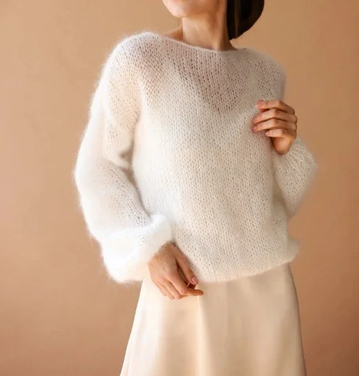 Braut trägt flauschigen, weißen Strickpullover kombiniert mit cremefarbener Satinhose oder Rock – moderner, minimalistischer Hochzeitsstil.