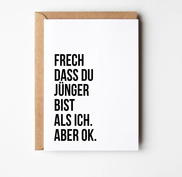 Humorvolle Geburtstagskarte mit dem Spruch: „Frech, dass du jünger bist als ich. Aber ok.“ in schwarzer Schrift auf weißem Hintergrund.