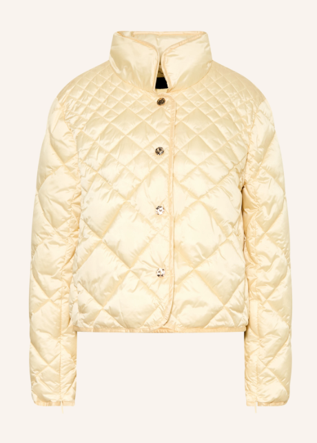 Hellgelbe gesteppte Übergangsjacke aus glänzendem Material mit hohem Stehkragen und vier auffälligen Schmuckknöpfen vor hellem Hintergrund. Kurze Steppjacke mit Rautenmuster, langen Ärmeln und verdecktem Verschluss.