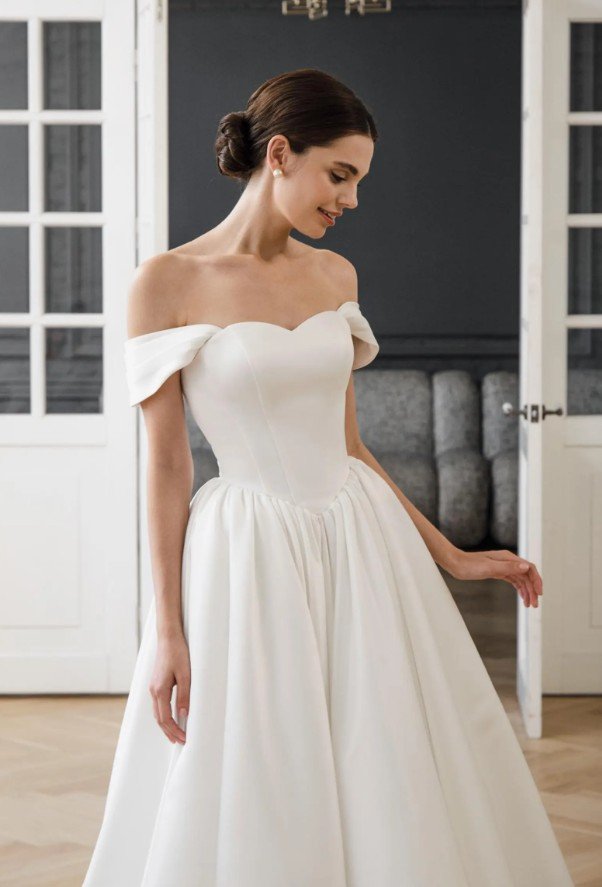 Elegantes, schulterfreies Brautkleid mit herzförmigem Ausschnitt und drapierten Off-Shoulder-Trägern, kombiniert mit einem weit schwingenden Rock in puristischem Weiß.