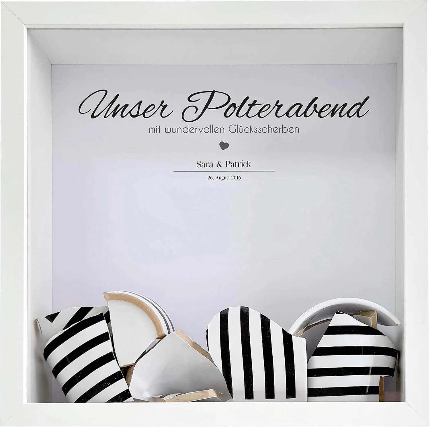 Ein weißer 3D-Bilderrahmen mit dem personalisierten Aufdruck „Unser Polterabend“, Namen und Datum. Im unteren Teil liegen als Erinnerungsstück einige zerbrochene Porzellanscherben.