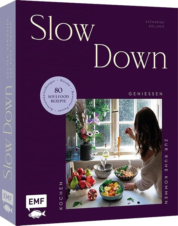 Violettes Buchcover „Slow Down“ von Katharina Küllmer. Es zeigt eine Frau am sonnigen Fenster mit gesundem Essen. Ein Siegel bewirbt 80 Soulfood Rezepte.