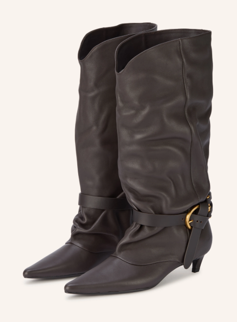 Ein Paar dunkelbraune Lederstiefel mit locker fallendem Schaft und spitzer Kappe sowie einem dekorativen Knöchelriemen mit goldener Schnalle vor hellem Hintergrund.