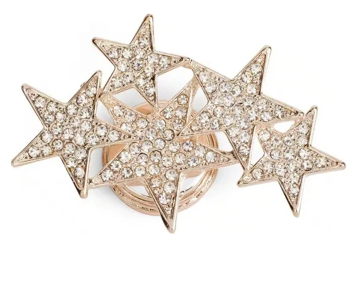 Nahaufnahme einer goldfarbenen Brosche, die aus fünf unterschiedlich großen, ineinander verschlungenen Sternen besteht. Jeder Stern ist vollständig mit kleinen, funkelnden weißen Kristallen besetzt. Hochwertiger Broschen Schmuck für elegante Outfits.