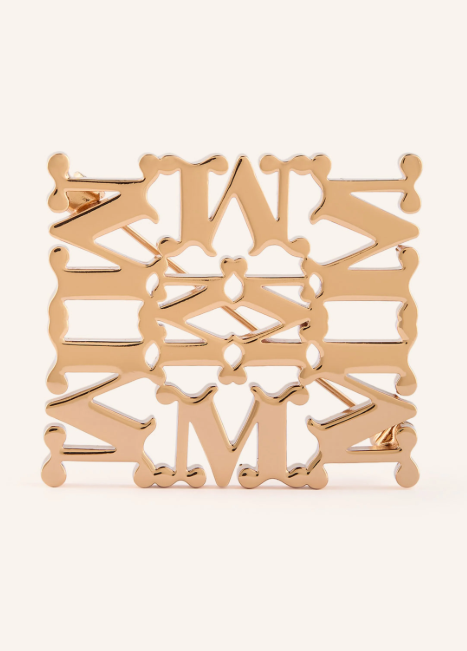 Eine quadratische, goldfarbene Brosche mit einem symmetrischen, durchbrochenen Muster aus sich wiederholenden „M“-Motiven.
