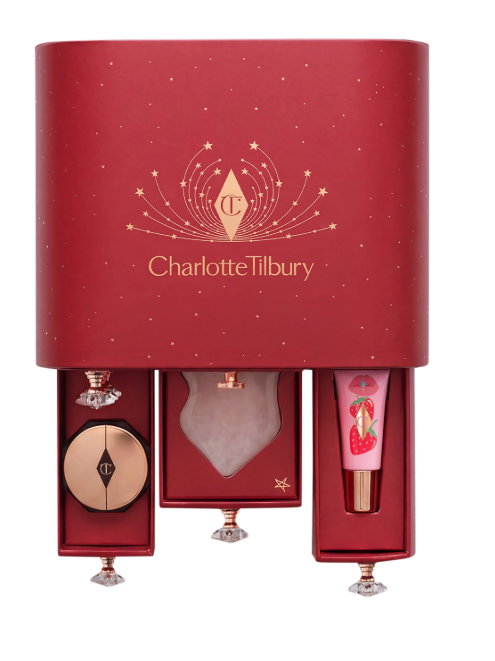 Dunkelroter Adventskalender von Charlotte Tilbury mit goldenem Logo und Sternenverzierungen. Im unteren Bereich sind drei Schubladen mit kristallförmigen Griffen herausgezogen, die einen Puder und einen Lipgloss mit Erdbeermotiv zeigen.