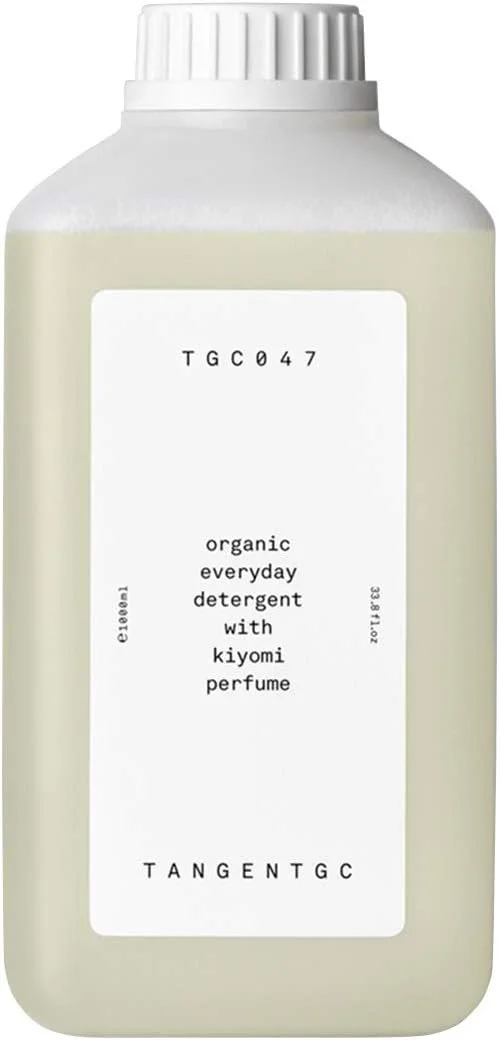 Eine eckige, halbtransparente Flasche mit weißem Verschluss, die ein hellgelbes, flüssiges Waschmittel enthält. Das minimalistische, weiße Etikett beschriftet das Produkt als „organic everyday detergent with kiyomi perfume“ der Marke TANGENTGC.