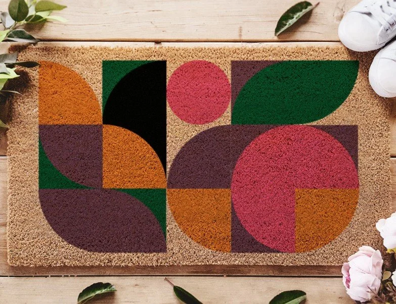 Rechteckige Kokos-Fußmatte mit einem modernen, geometrischen Muster aus bunten Formen (Halbkreise und Kreise) in Terrakotta, Dunkelgrün, Pink und Schwarz.