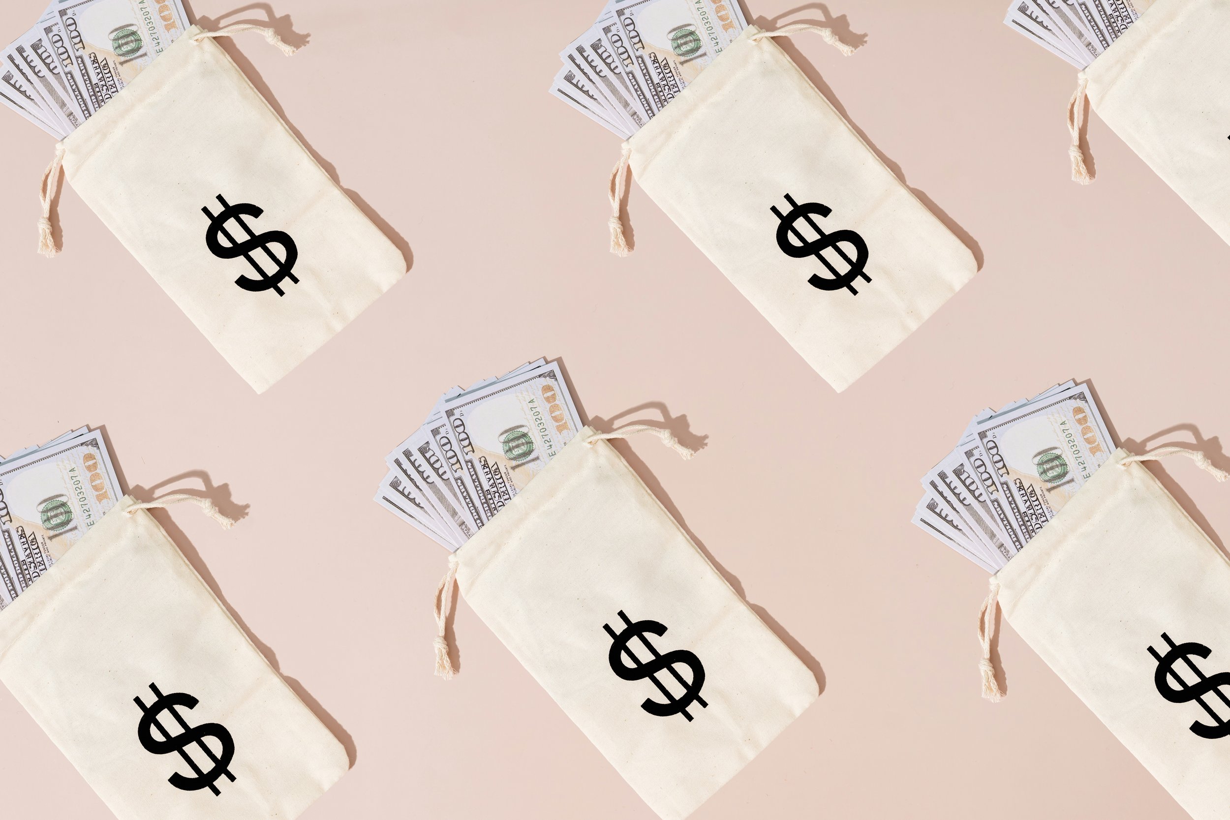 Ästhetisches Flatlay auf beigem Hintergrund: Mehrere kleine Stoffsäckchen mit Dollar-Zeichen, aus denen Geldscheine herausschauen – als Symbol für stilvolle Geldgeschenke zur Hochzeit.